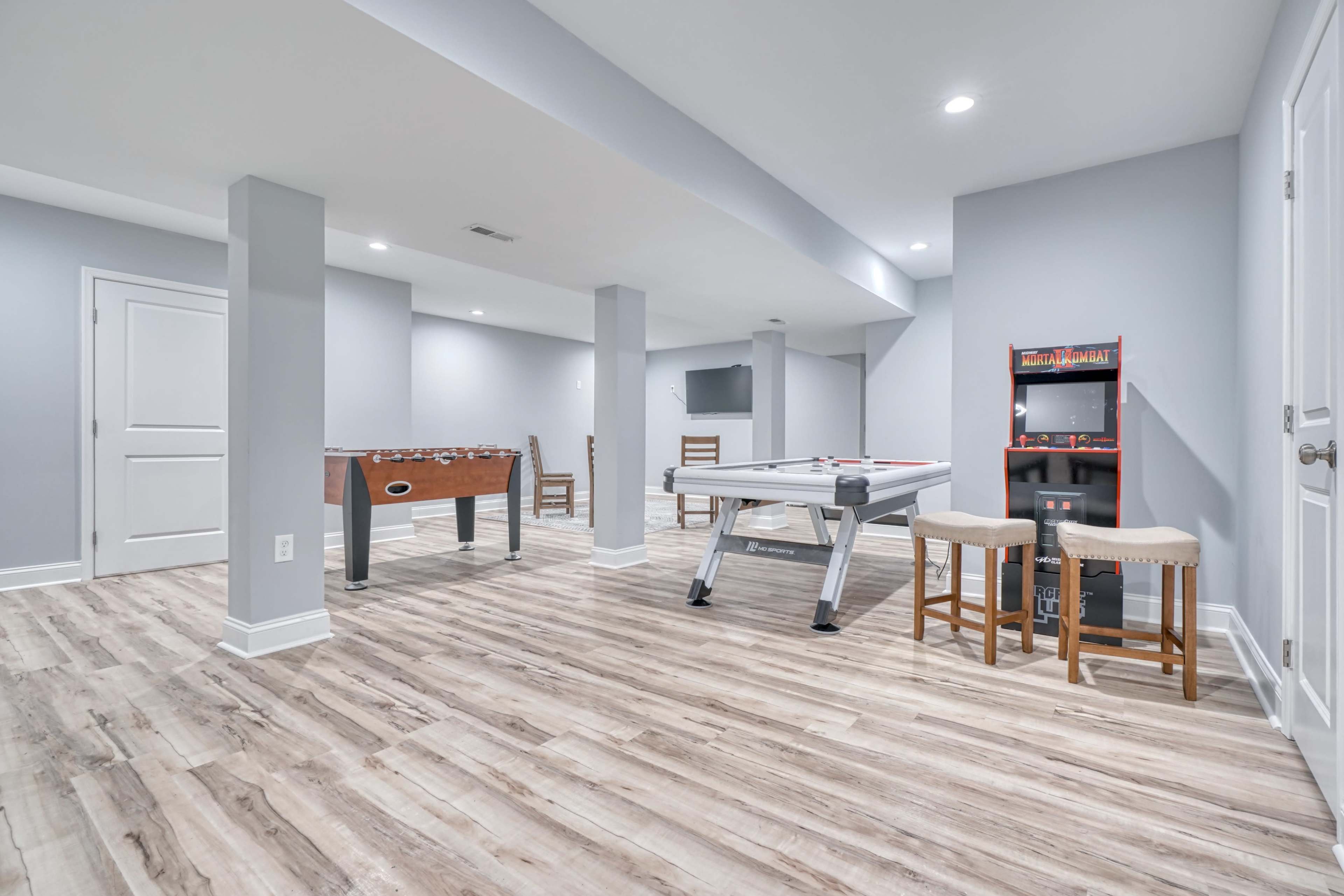 A spacious, finished basement with a foosball table, a pool table, and seating arranged near a small arcade cabinet.