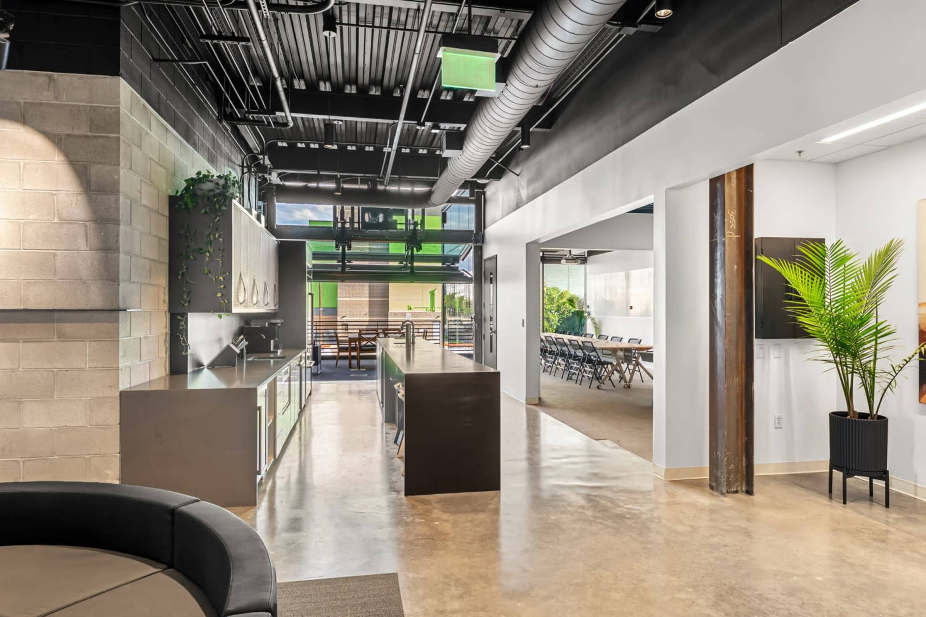 The image shows a modern office space featuring an open layout with a kitchen area, seating, and a meeting area separated by partitions.