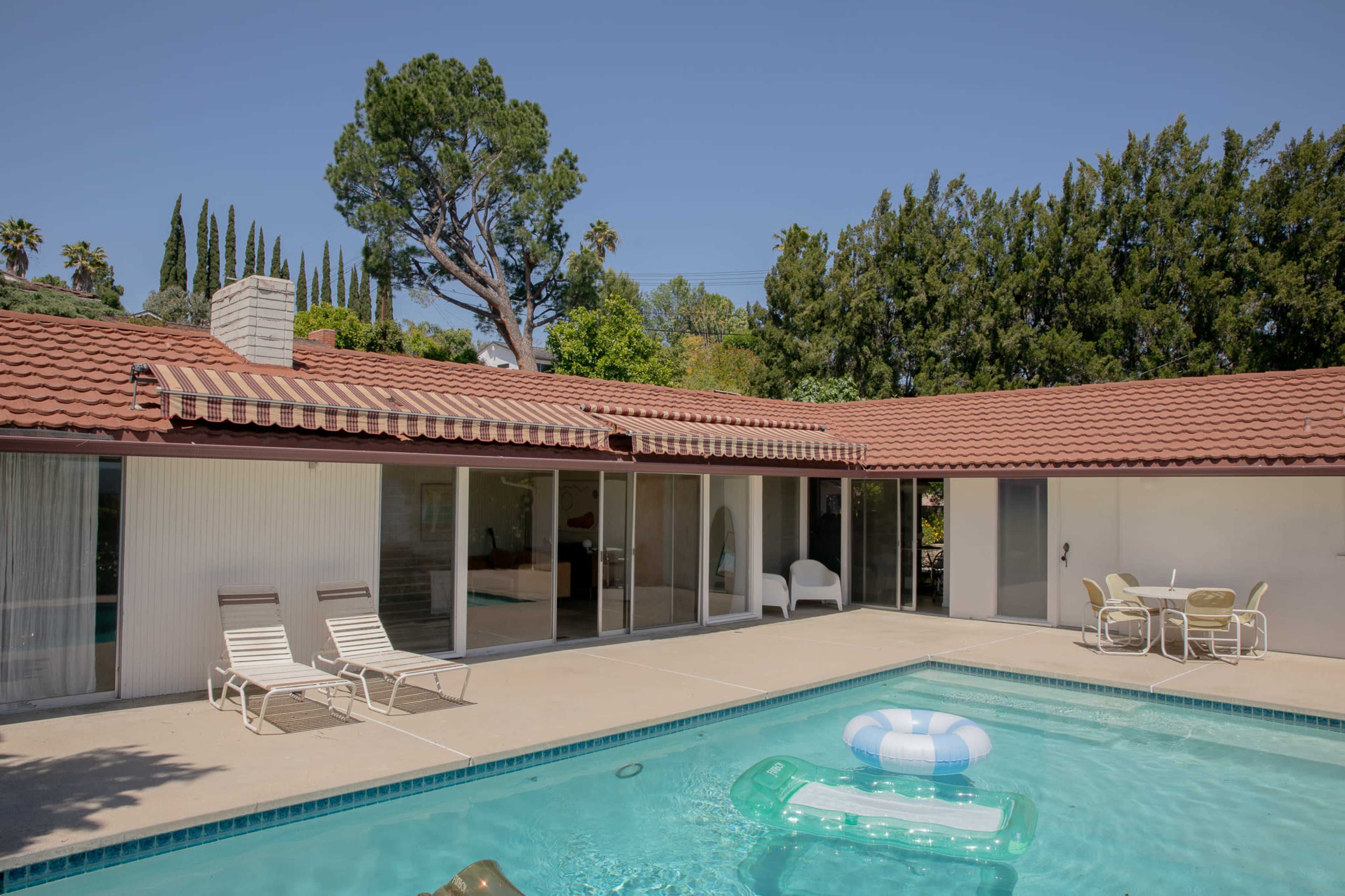A modern home features a swimming pool with a lounge area and outdoor furniture under clear blue skies.
