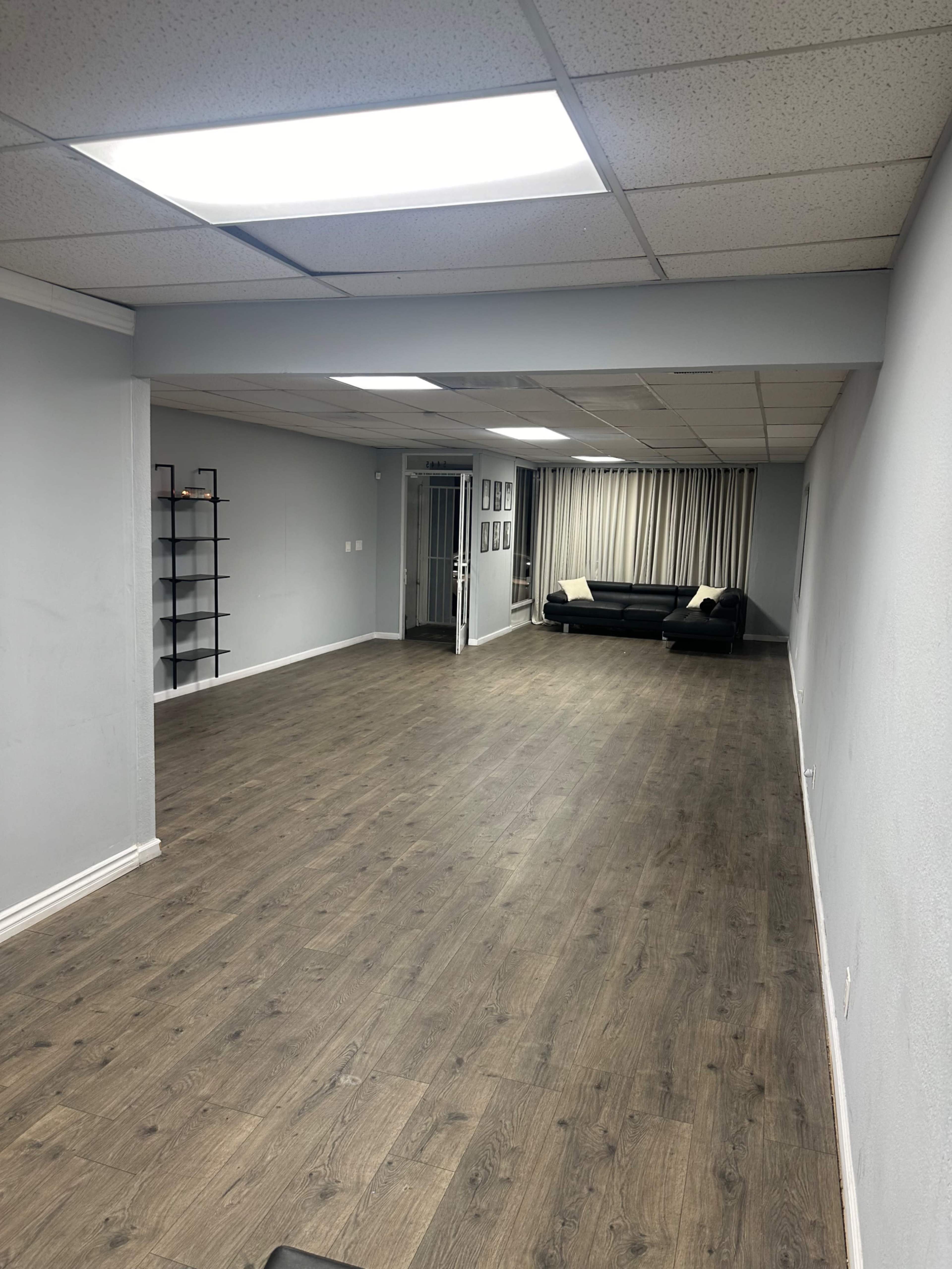 The image shows a spacious, empty room with a wooden floor, gray walls, and a black couch against one wall.