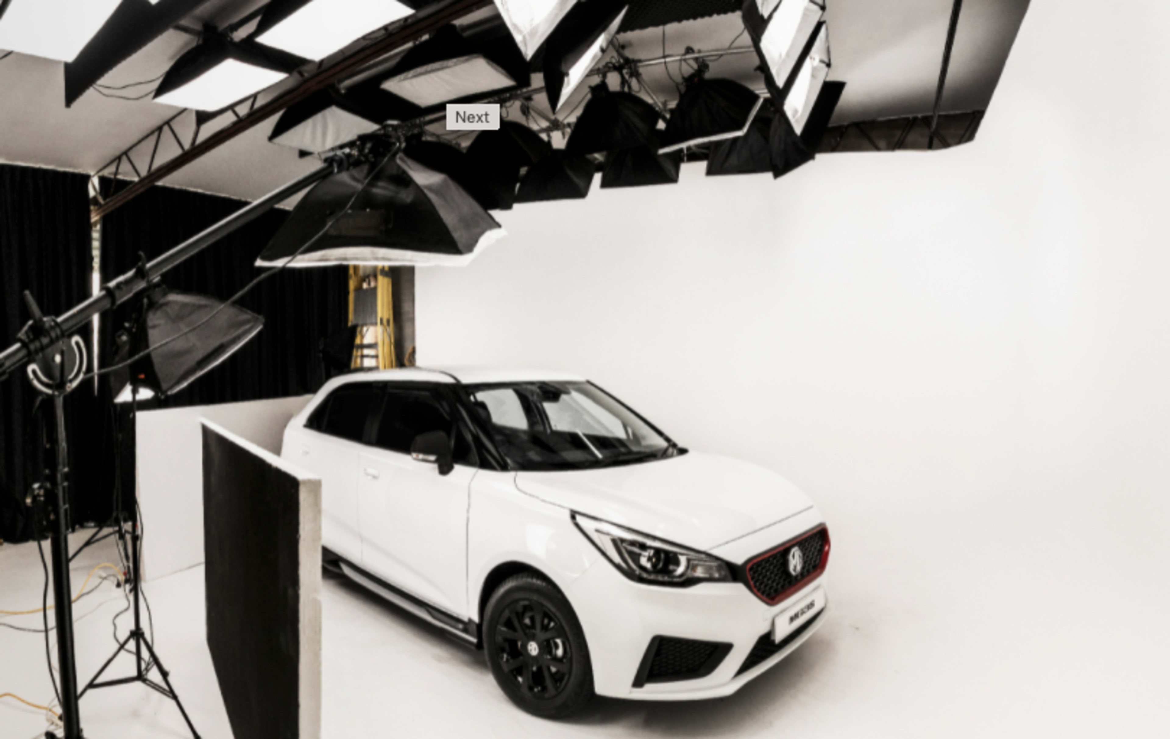 A white car is positioned in a brightly lit photography studio with softbox lights and a plain white backdrop.