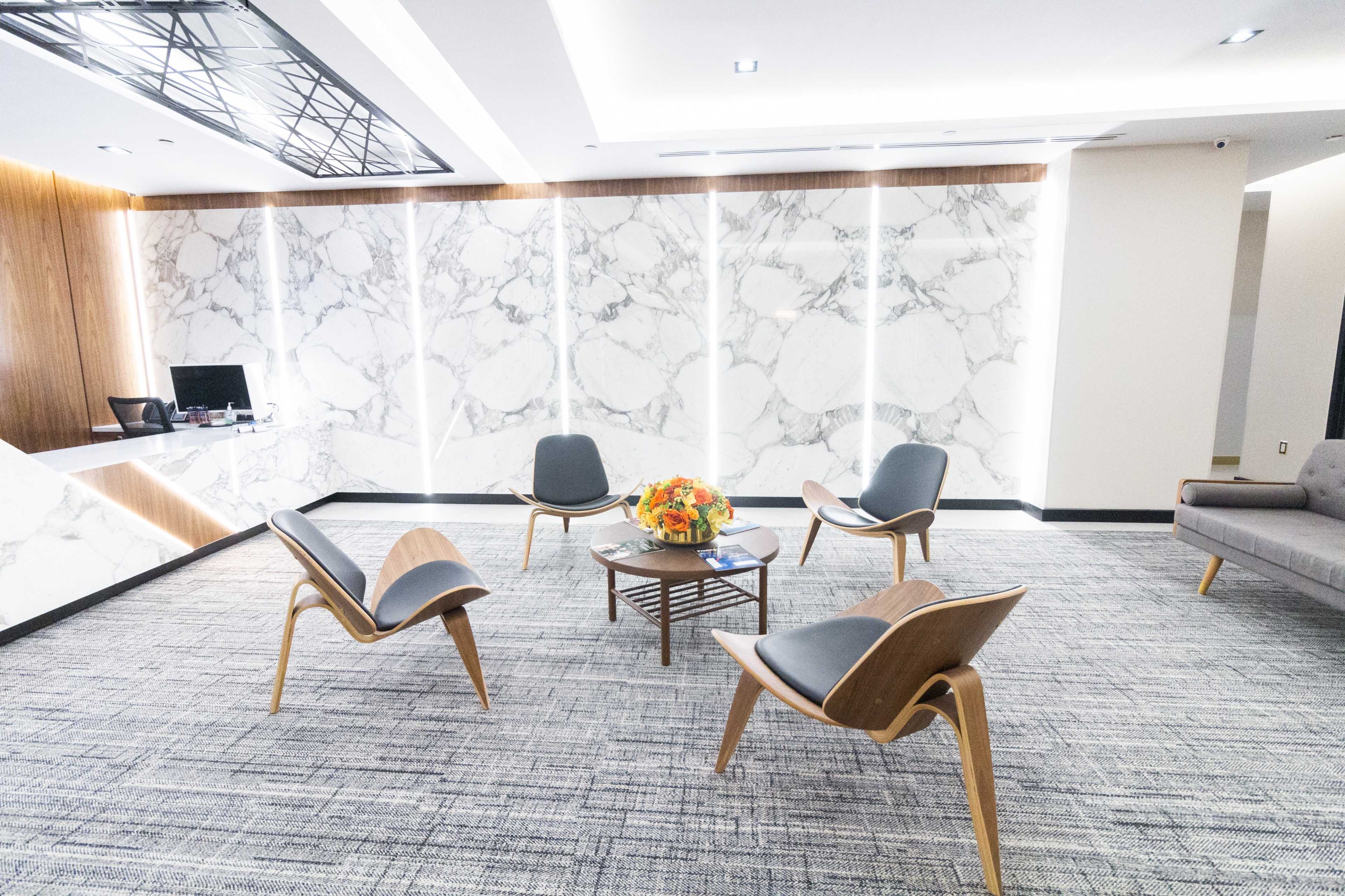The image shows a modern waiting area with four wooden chairs arranged around a central coffee table, set against a marble wall backdrop.