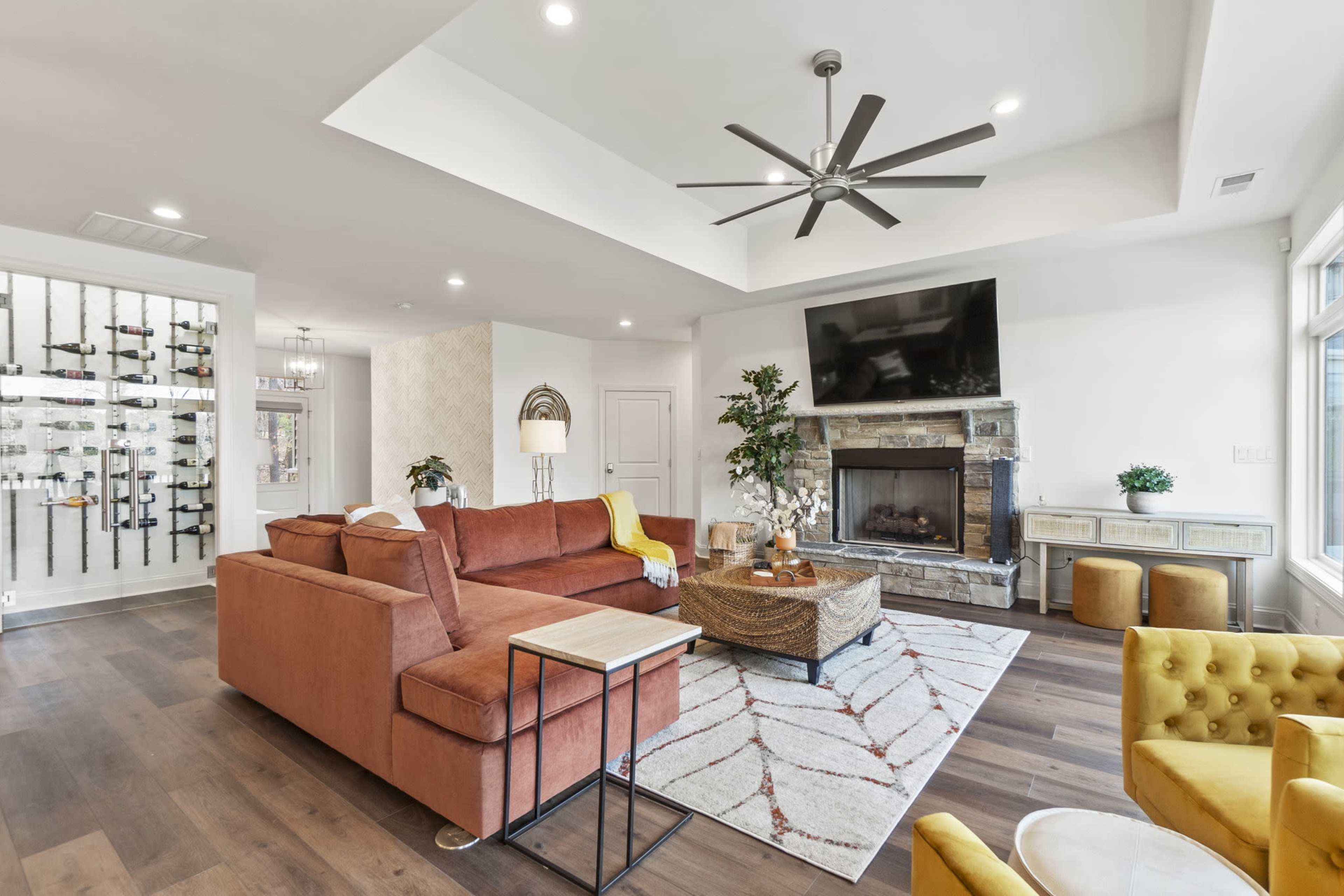 The living room features a brown sectional sofa, a stone fireplace with a television above it, and a wet bar with wine storage in the background.