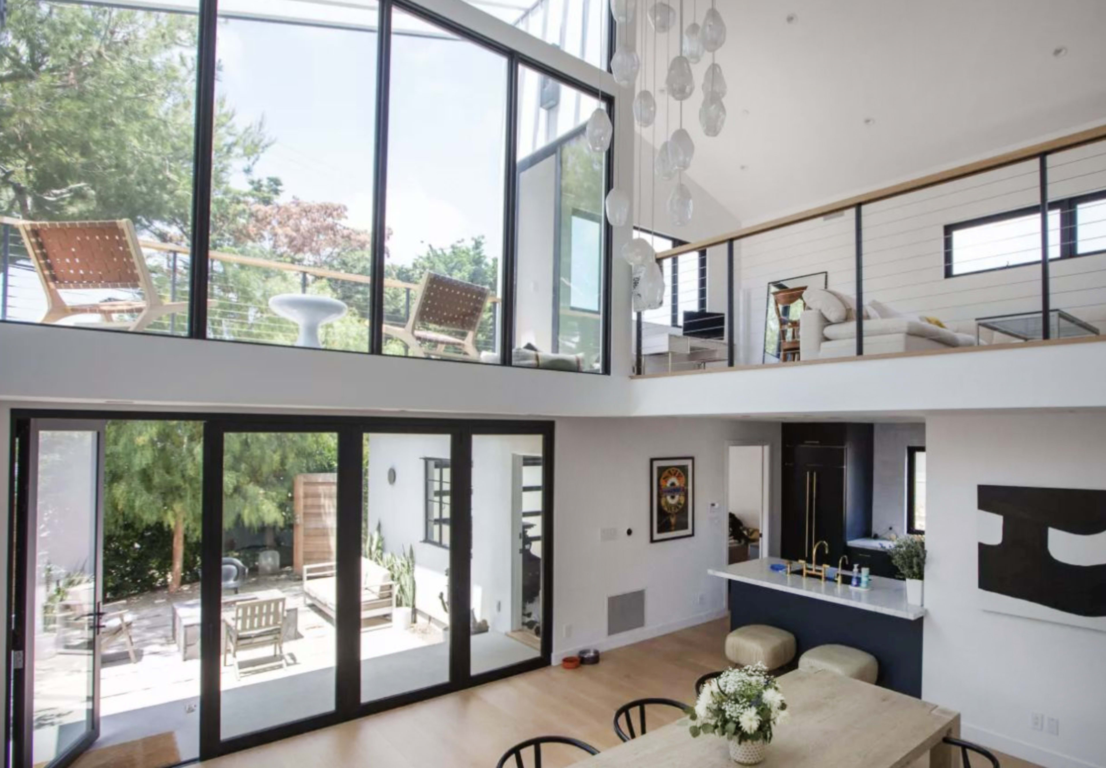 A modern, open-concept living area with large glass windows, a balcony on the upper level, and a view of an outdoor patio.