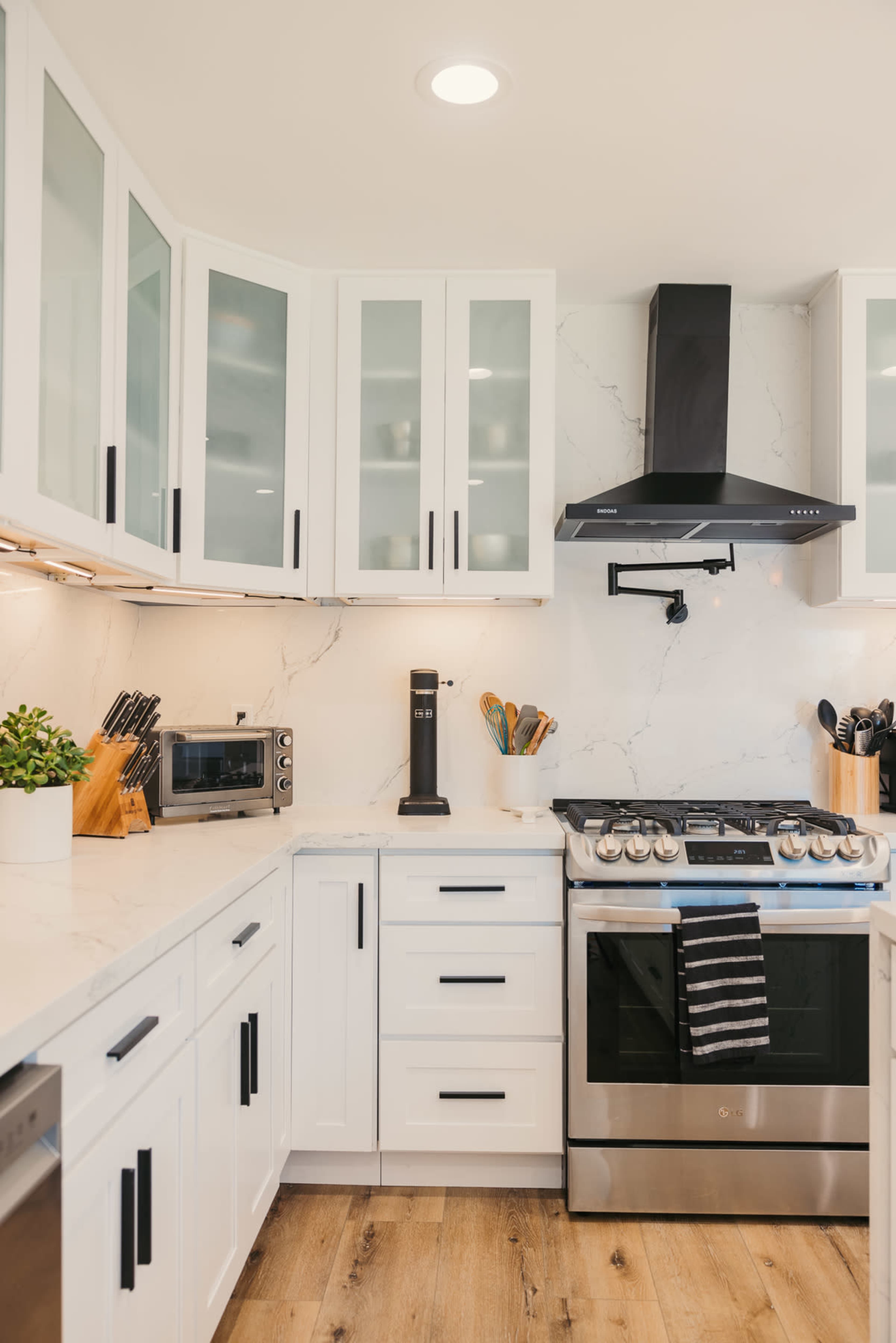 A modern kitchen features white cabinetry, a black range hood, stainless steel appliances, and marble countertops.