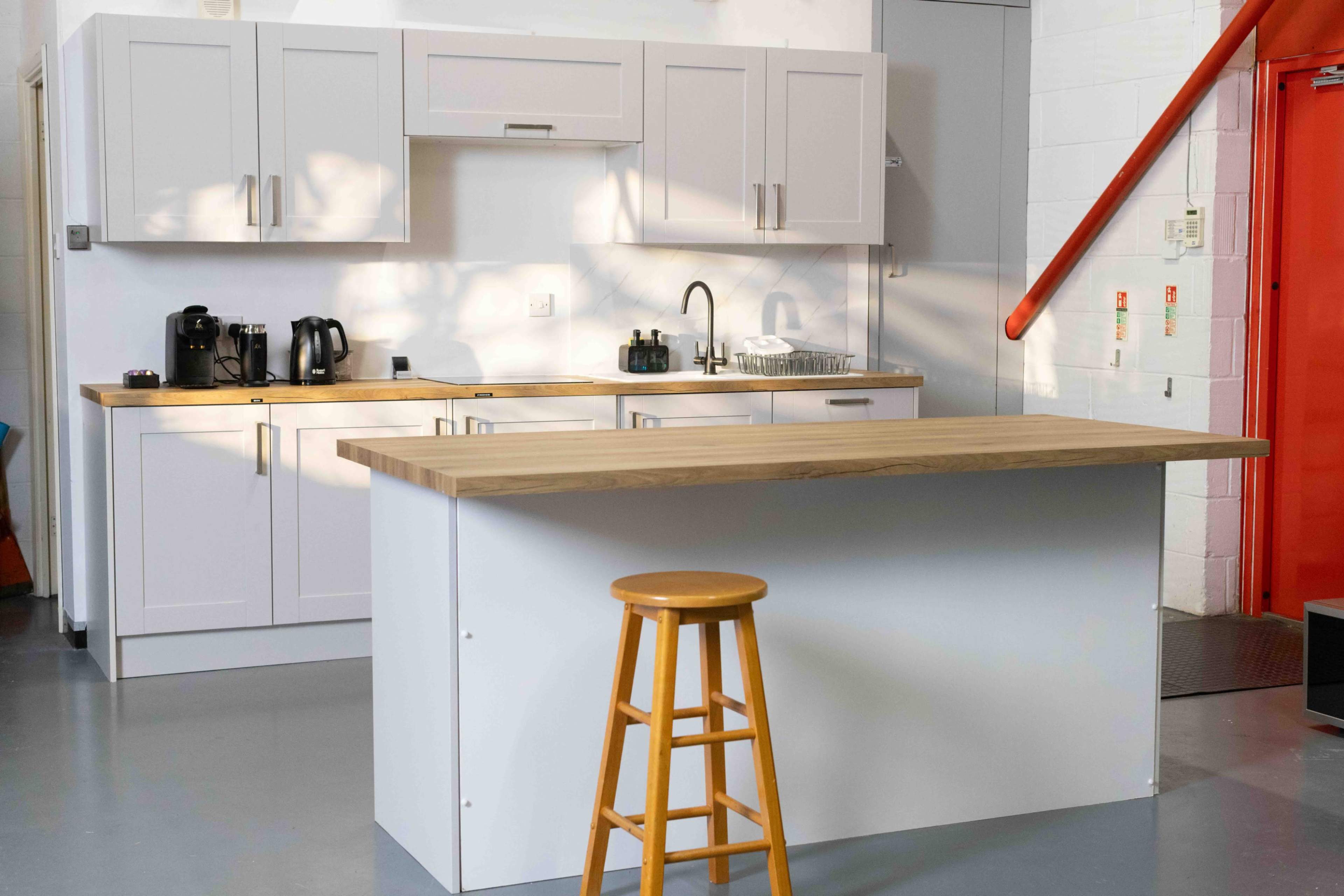 The image shows a modern kitchen with white cabinetry, a wooden countertop island, a stool, and stainless steel appliances.