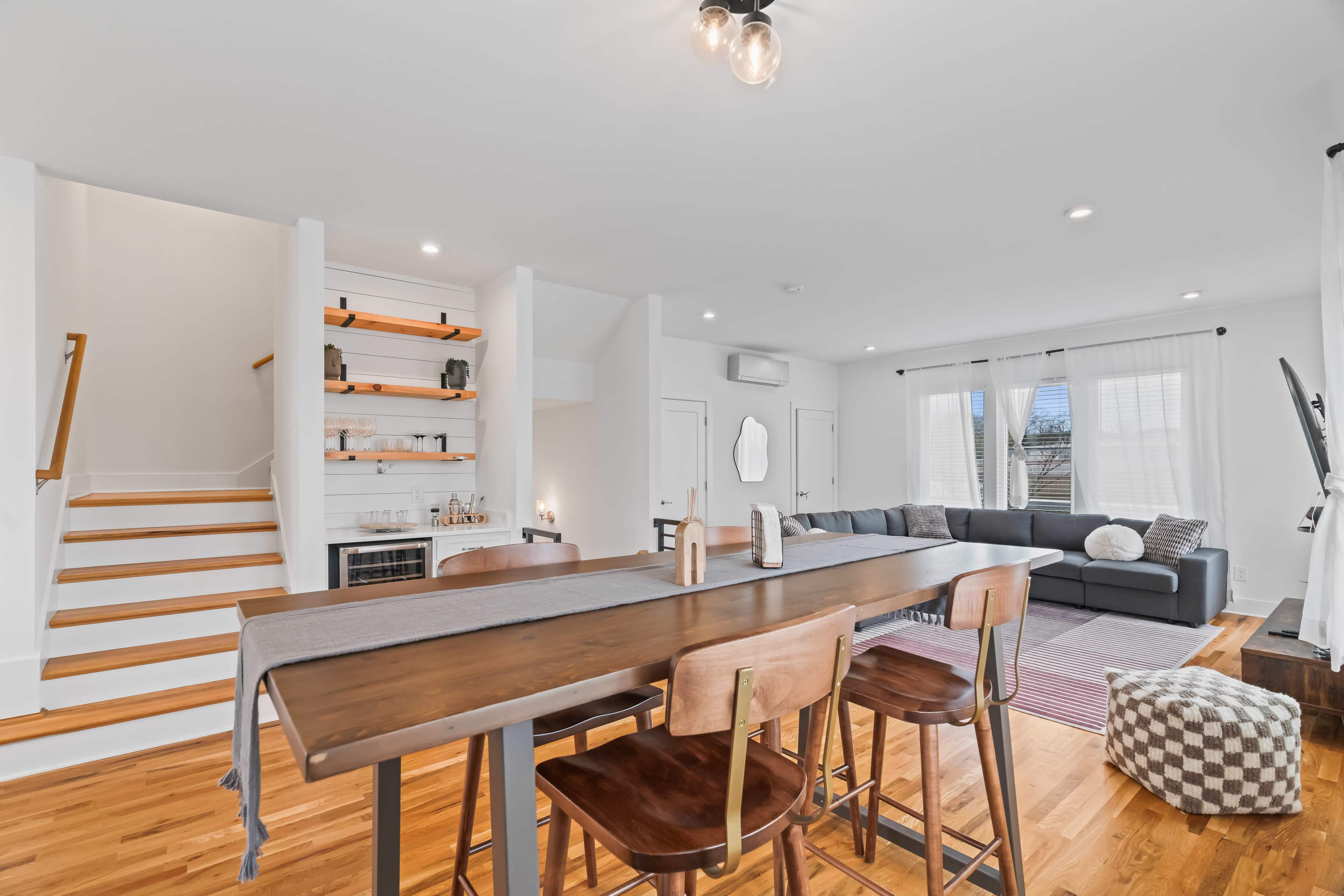 A modern living room features a large sectional sofa and a dining area with a long wooden table and high-backed chairs.