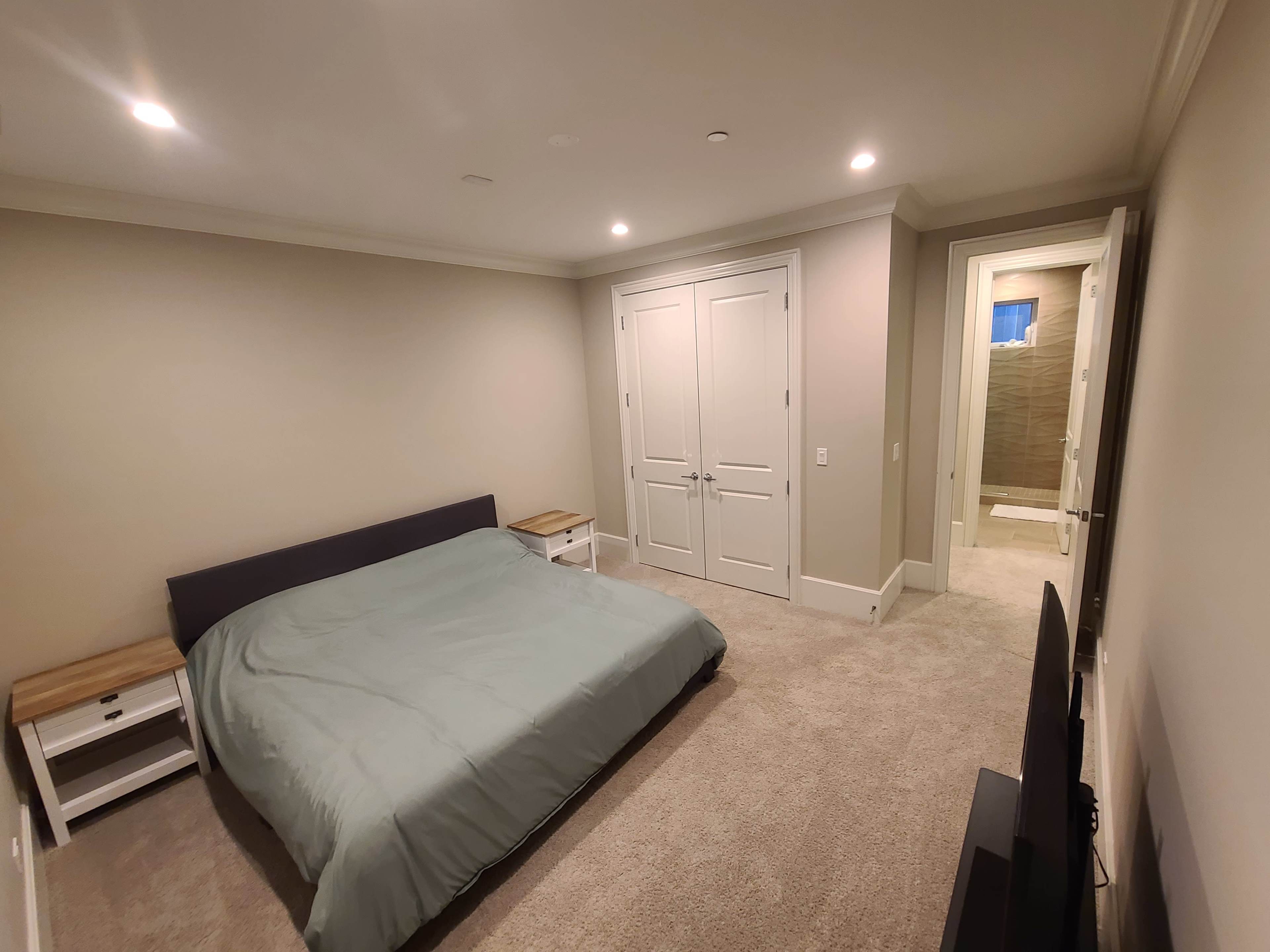 A spacious bedroom with a large bed, two nightstands, and an adjoining bathroom visible through an open door.