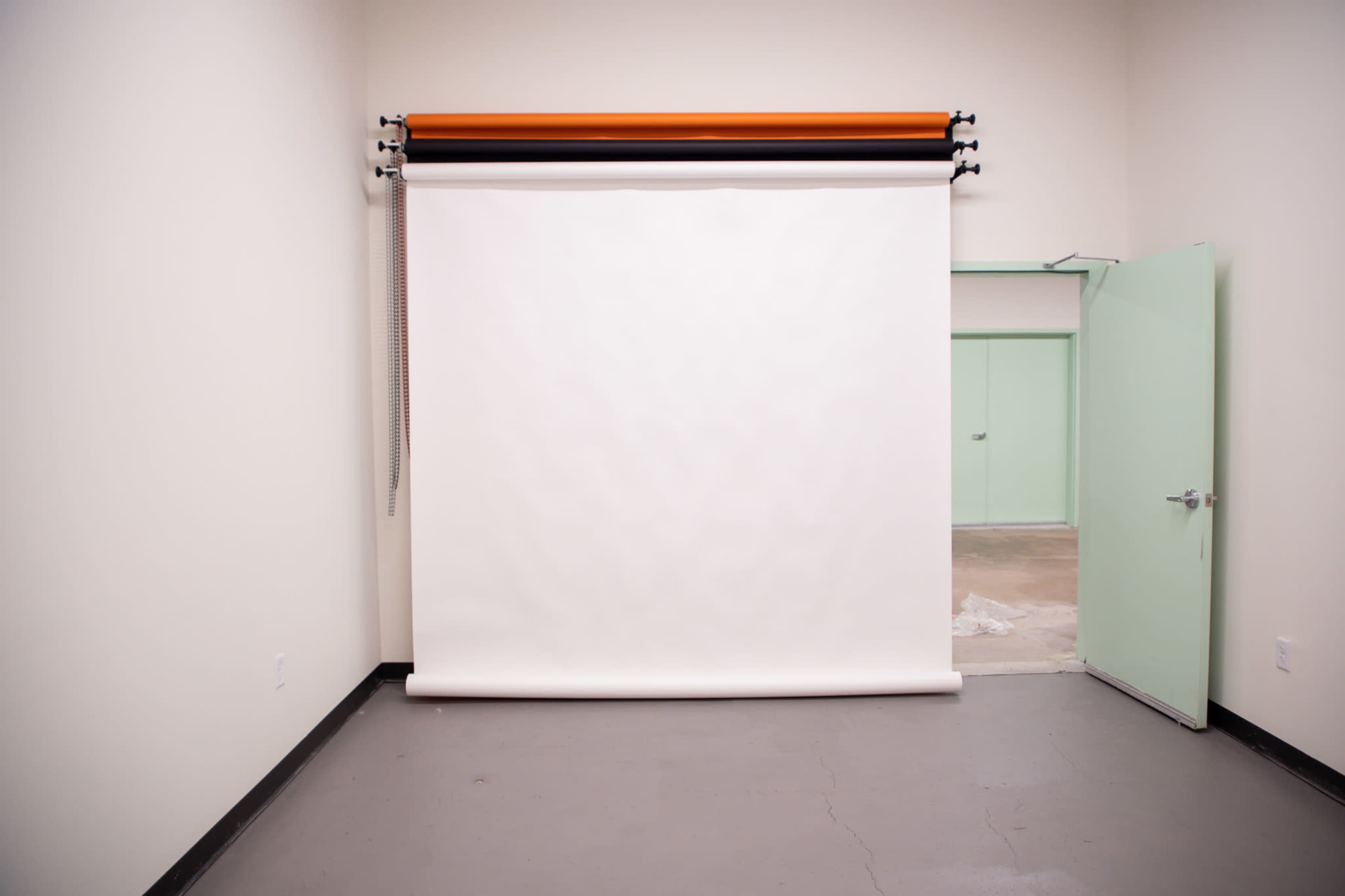 A minimalistic photography studio with a white backdrop, a green door to the left, and a concrete floor.