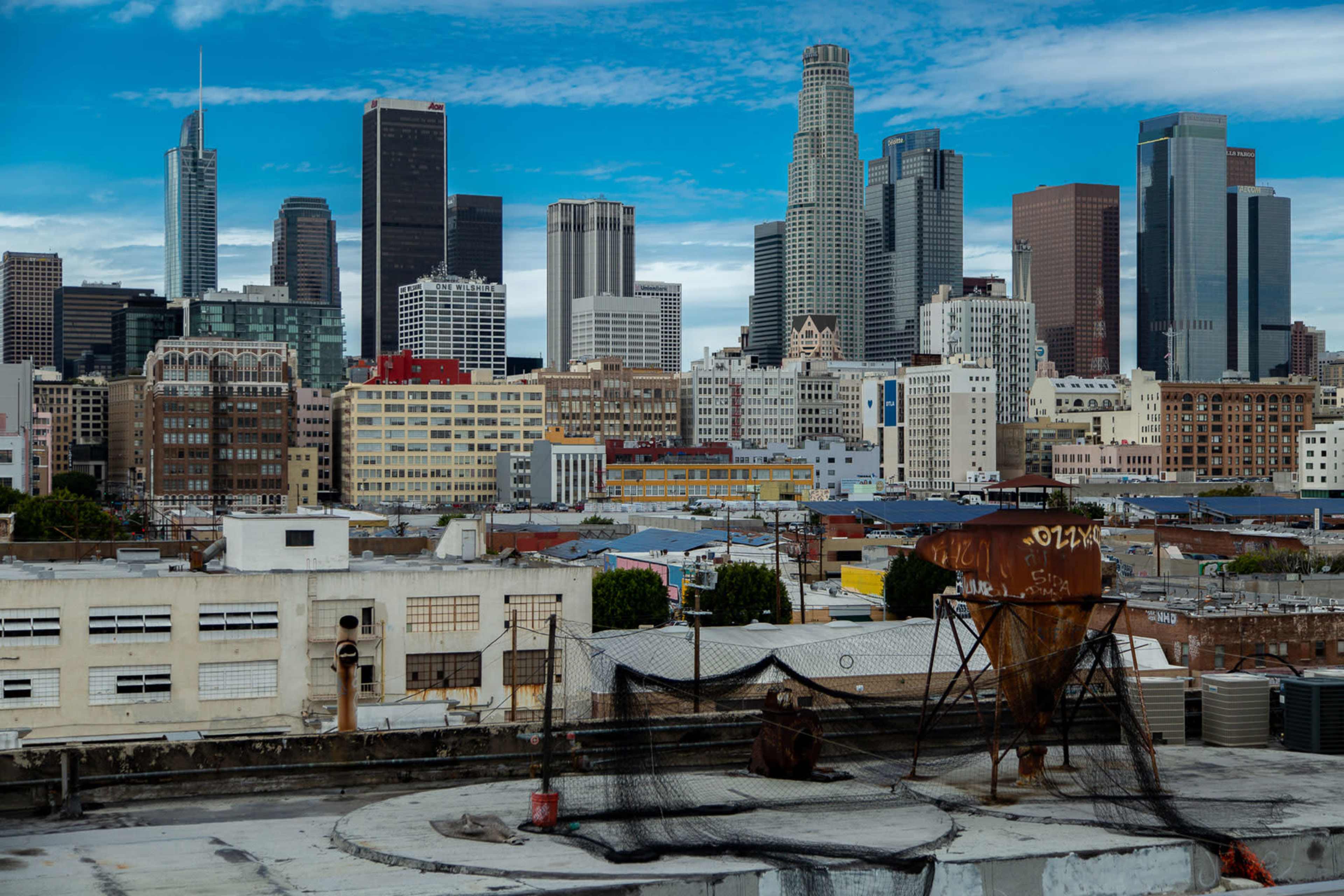 A view of downtown Los Angeles showcases a skyline of modern skyscrapers with a mix of older buildings and industrial structures in the foreground.