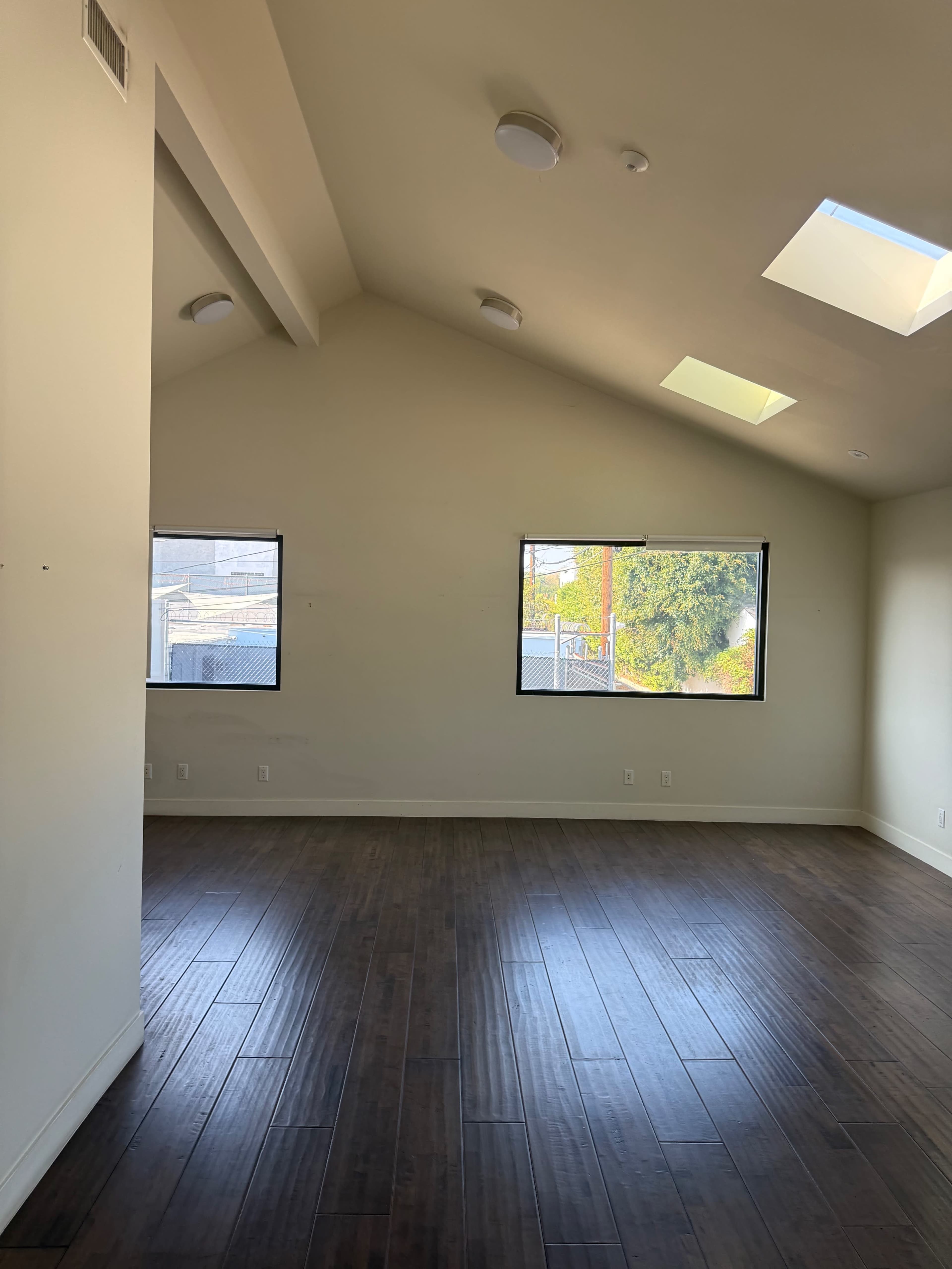 A spacious room with a high ceiling features two windows and skylights, and has wooden flooring.