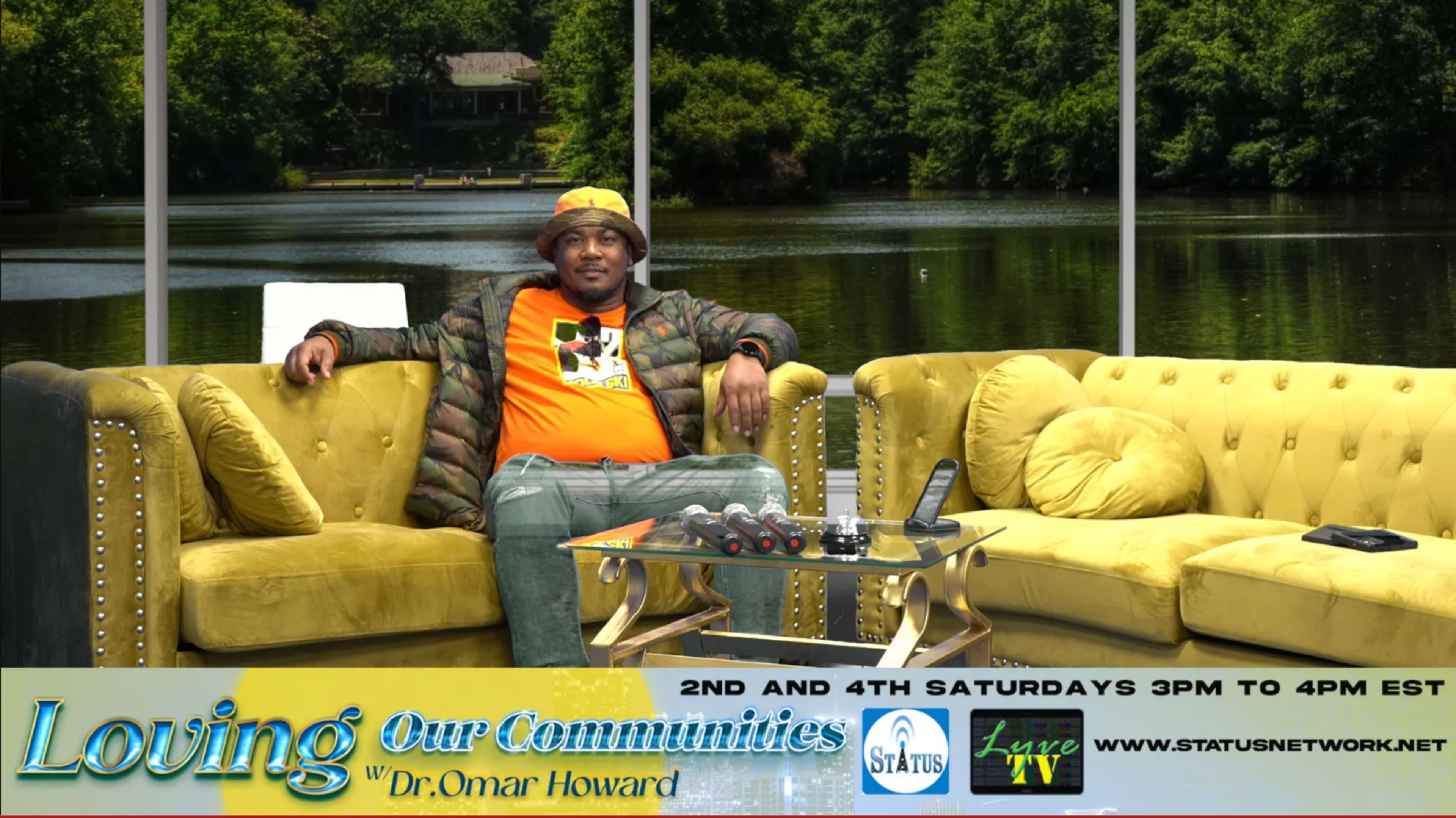 A man sits on a yellow couch in a studio with a view of a lake and greenery outside.