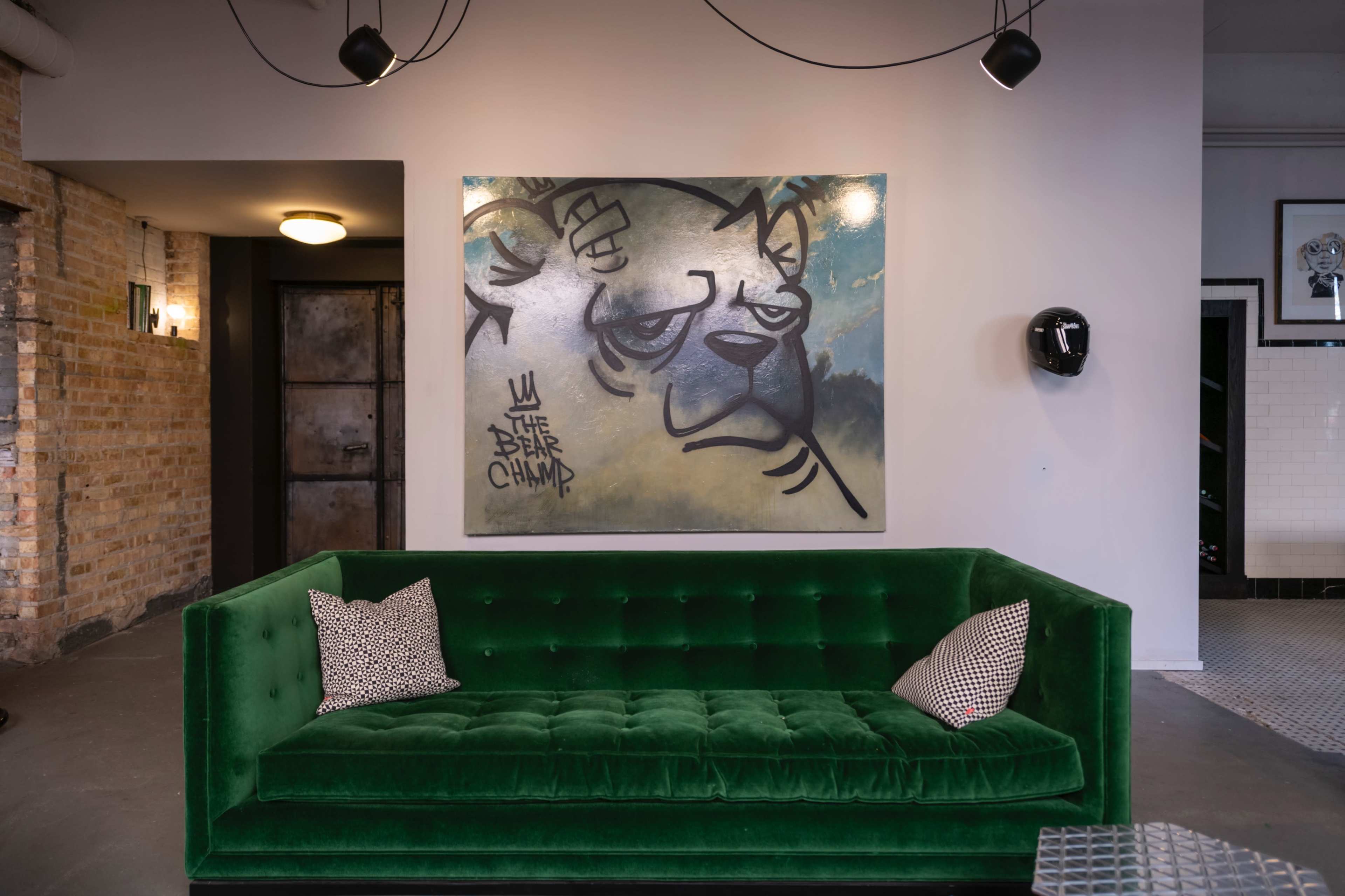 A green velvet couch with two patterned pillows is positioned against a wall featuring a large mural of a bear.