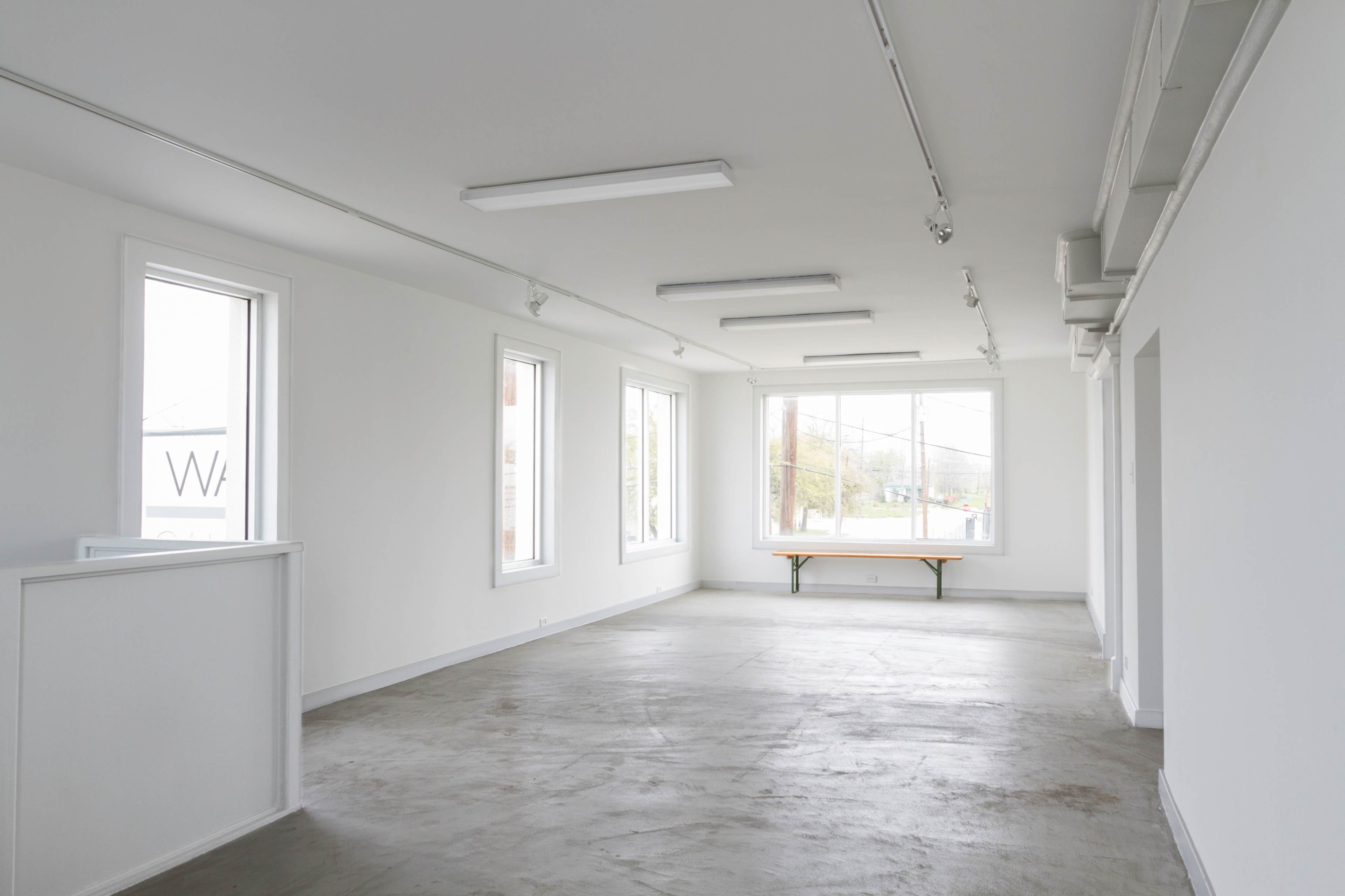 The image shows a vacant room with white walls, several windows, and a wooden table near the window.