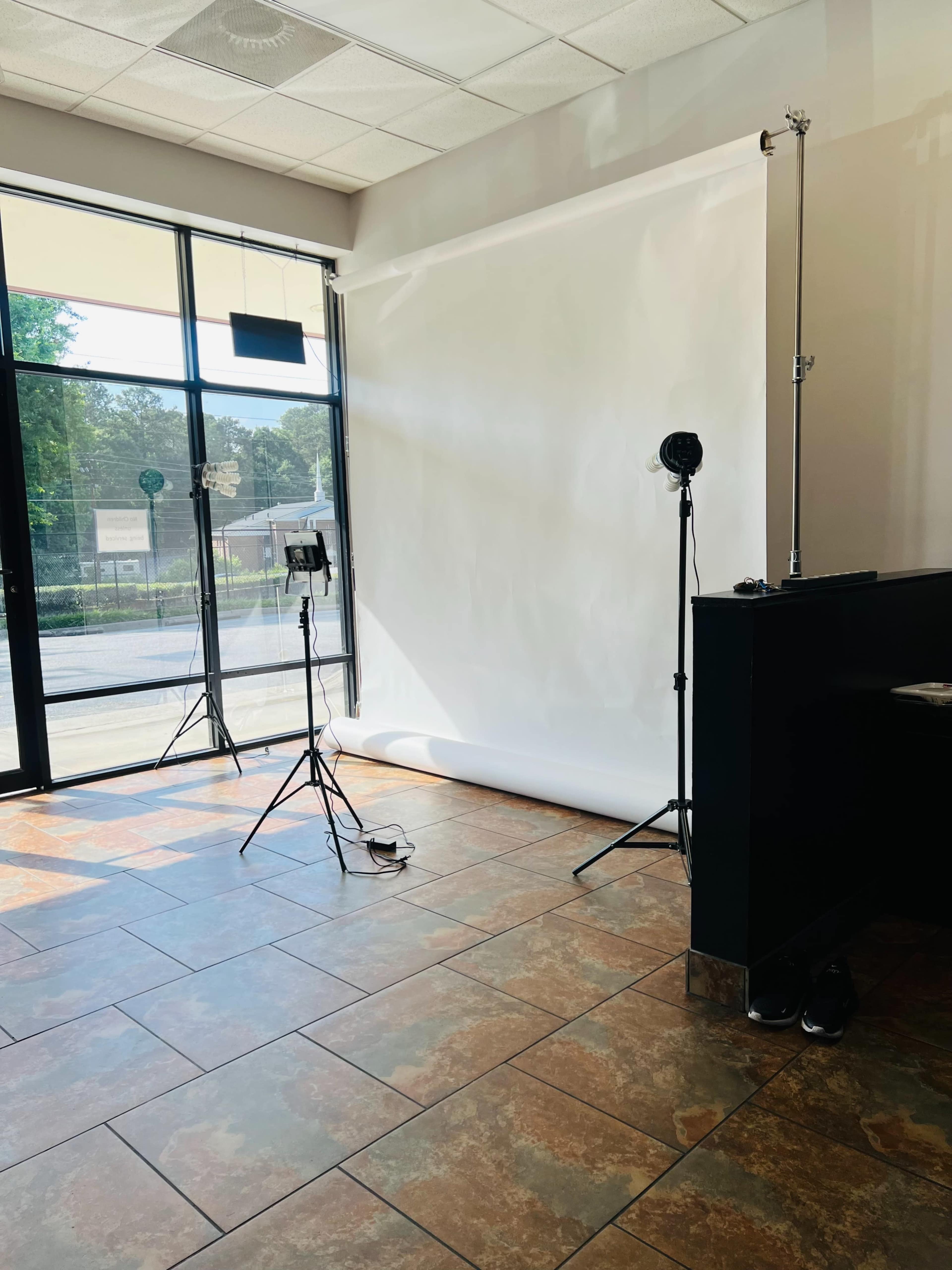 The image shows a well-lit studio space featuring a plain white backdrop, two lighting stands, and a tiled floor.