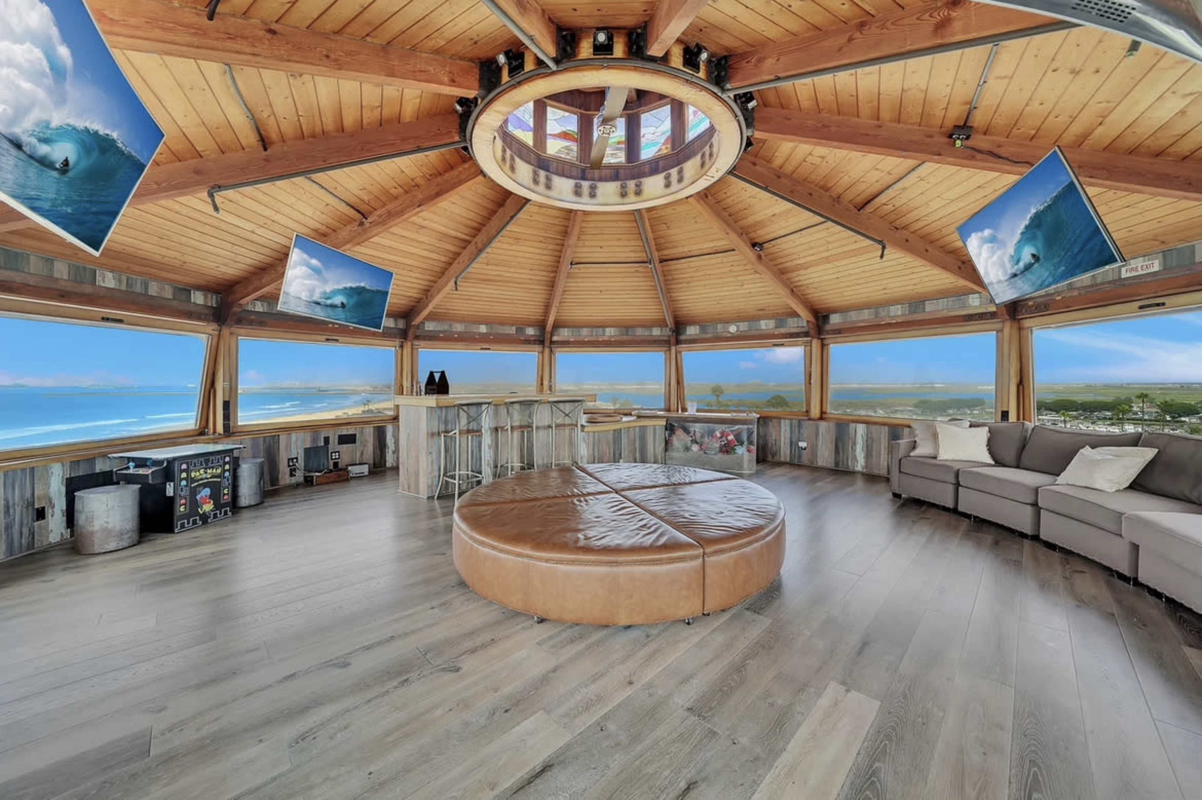 A circular, wooden interior with large windows offering a panoramic view, a bar area, and multiple screens mounted on the walls.