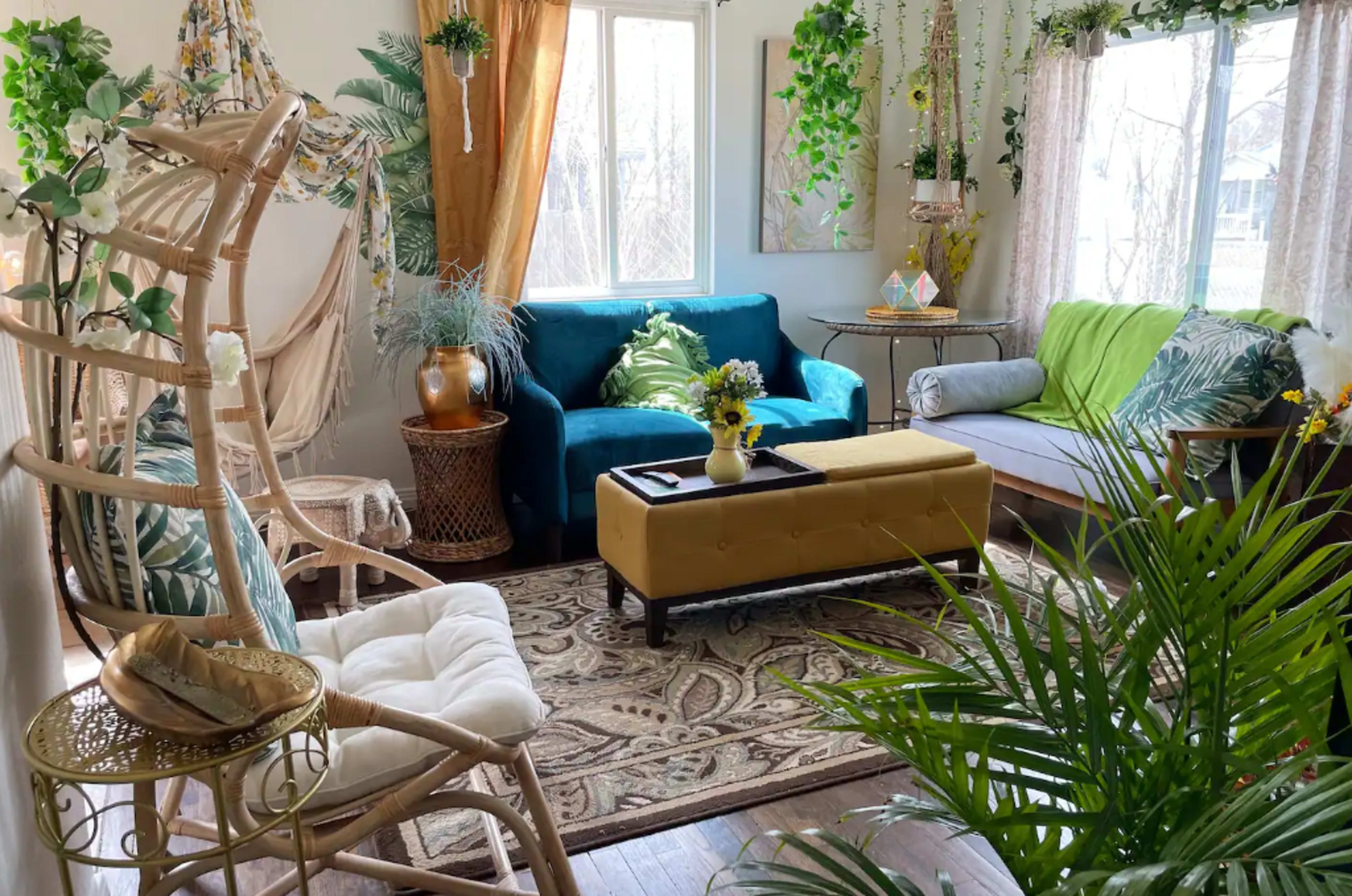 A sunlit living room adorned with plants, a blue sofa, a gray seating area, and eclectic decorative elements.