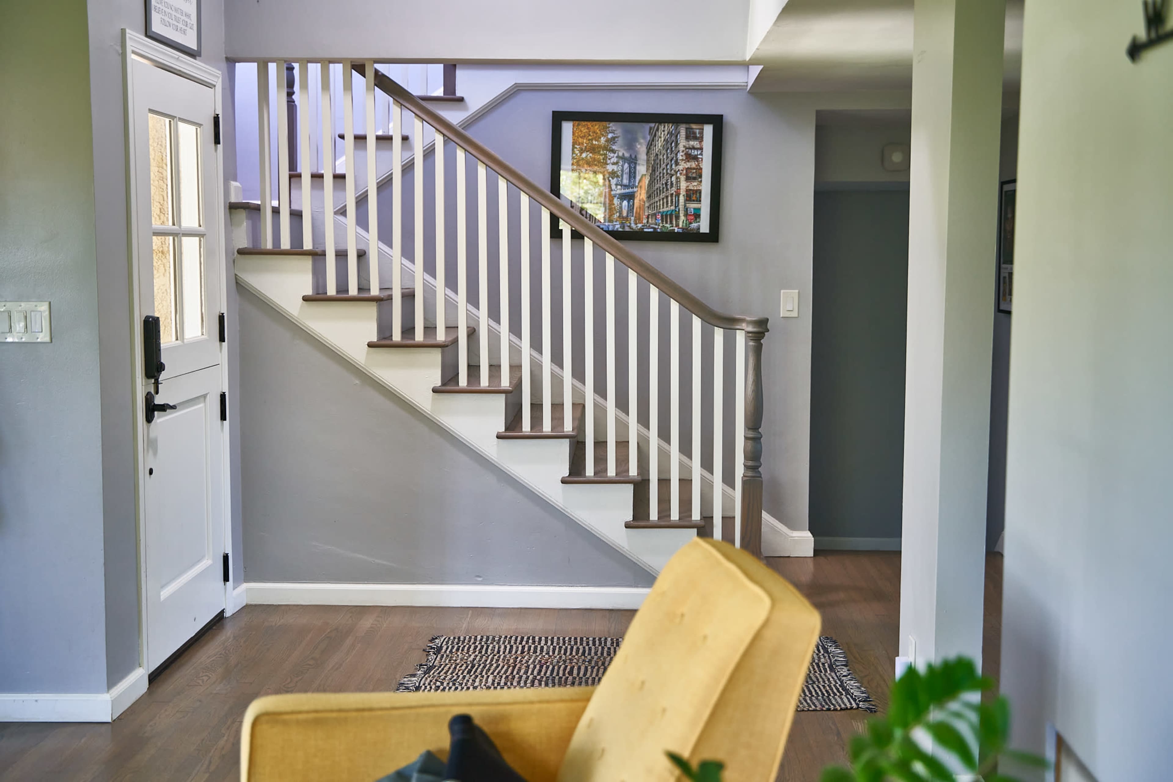 The image shows a staircase with white railings leading to an upper floor, adjacent to a door and a framed picture on the wall.