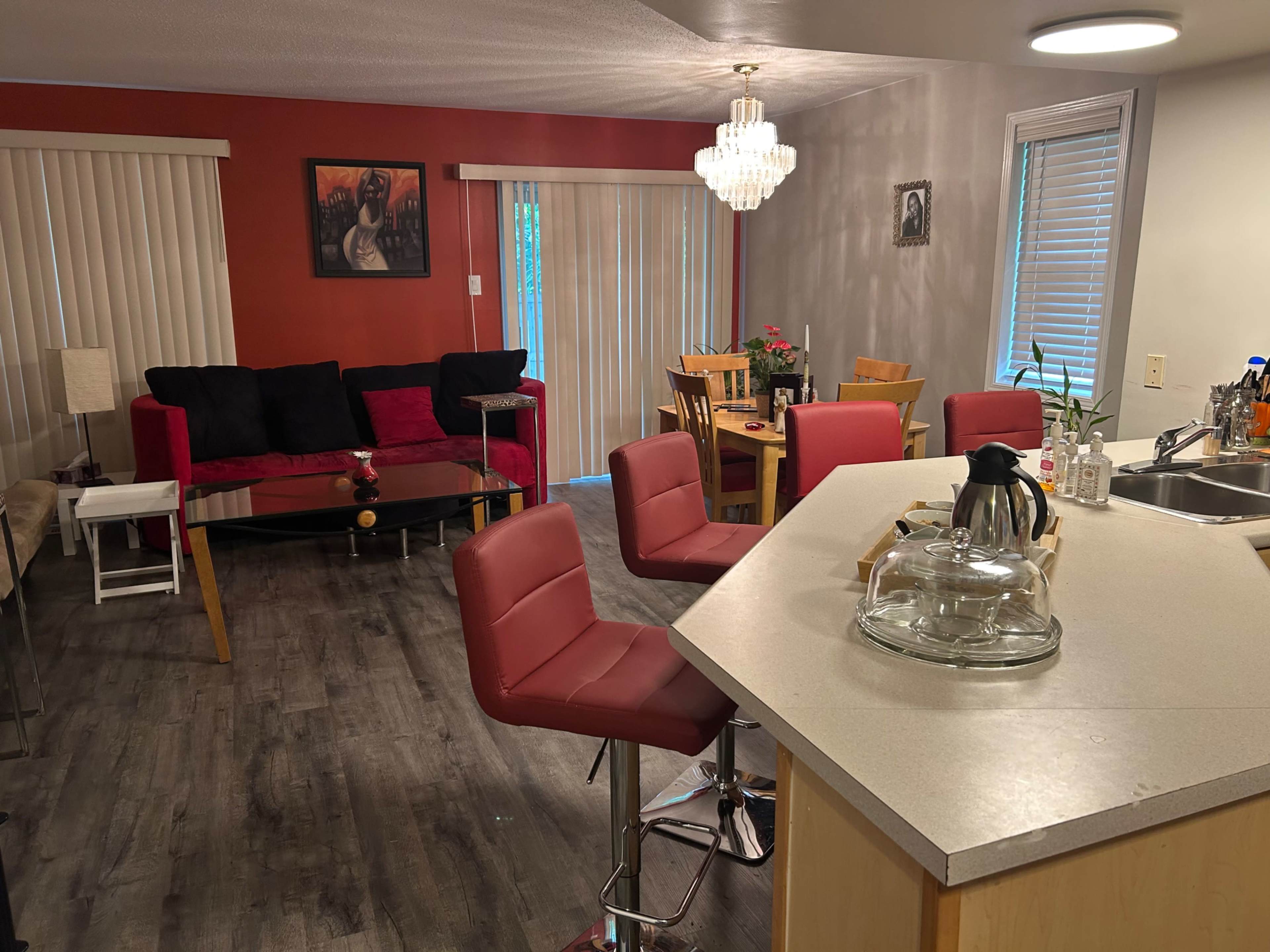 A cozy living area and kitchen with a modern layout, featuring red and neutral tones, seating arrangements, and a dining table.