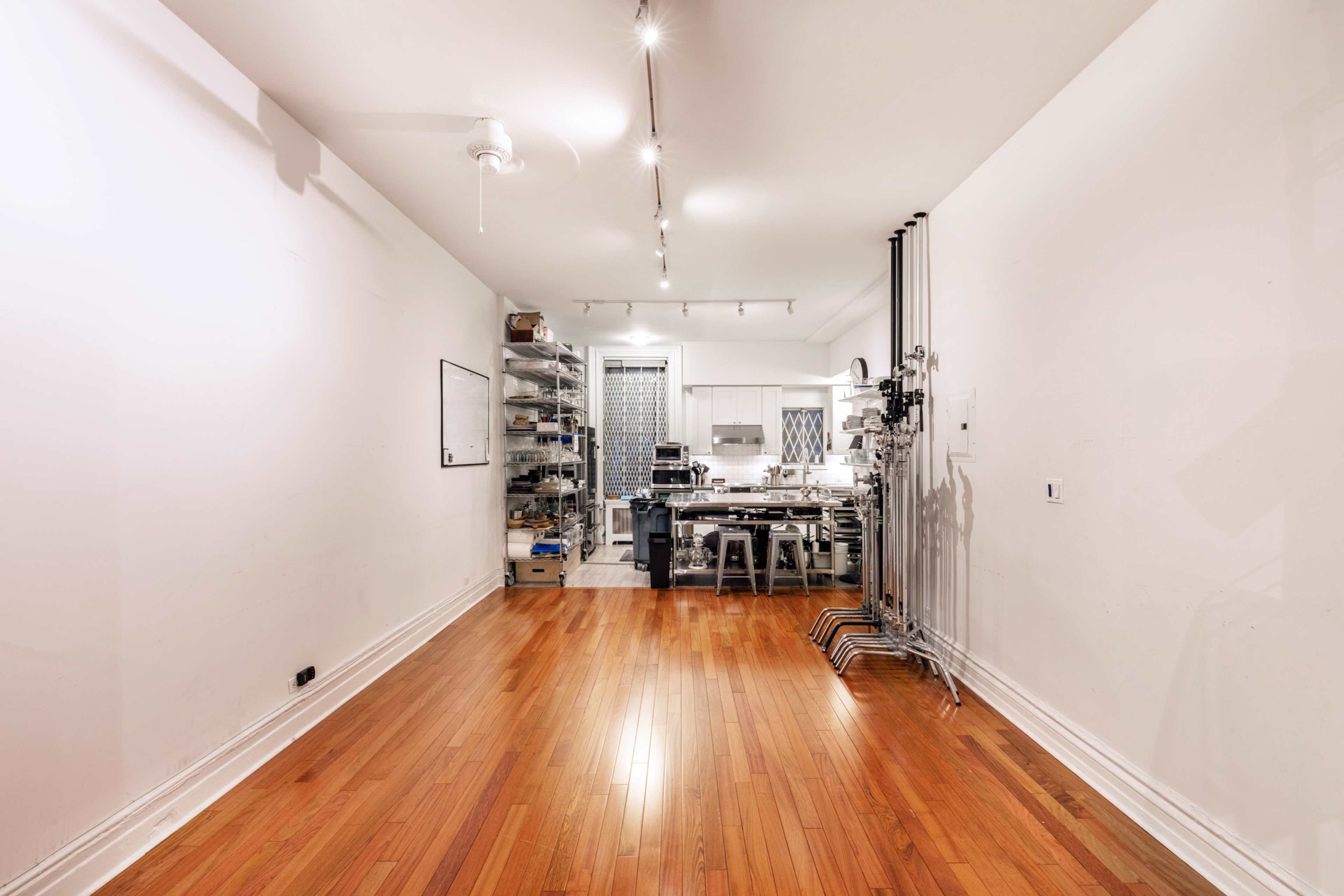 A spacious room with hardwood flooring features a kitchen area against one wall and storage shelves on the opposite side.