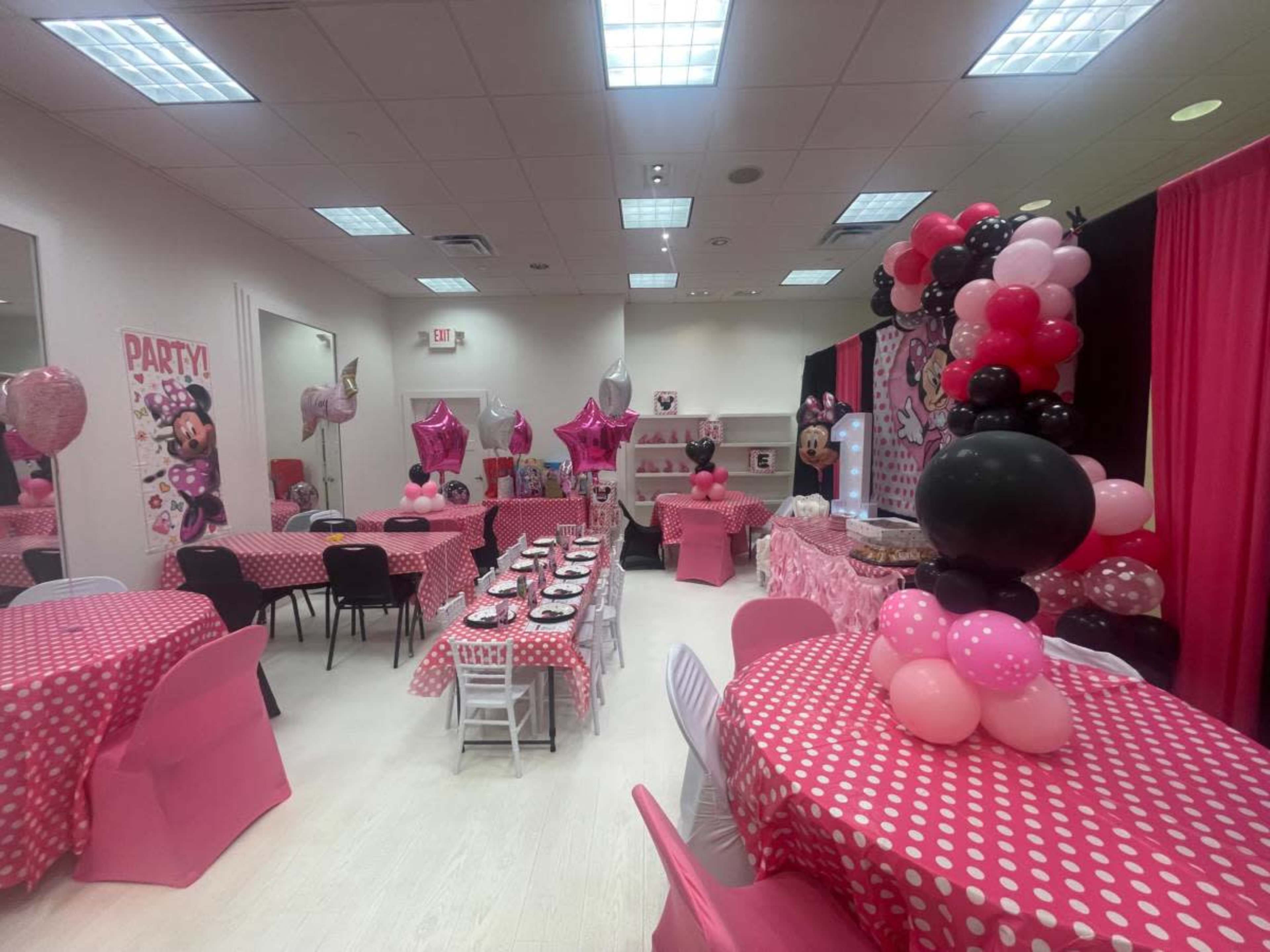The image shows a decorated party room with pink and black balloons, tables covered in polka dot tablecloths, and party supplies arranged for a celebration.