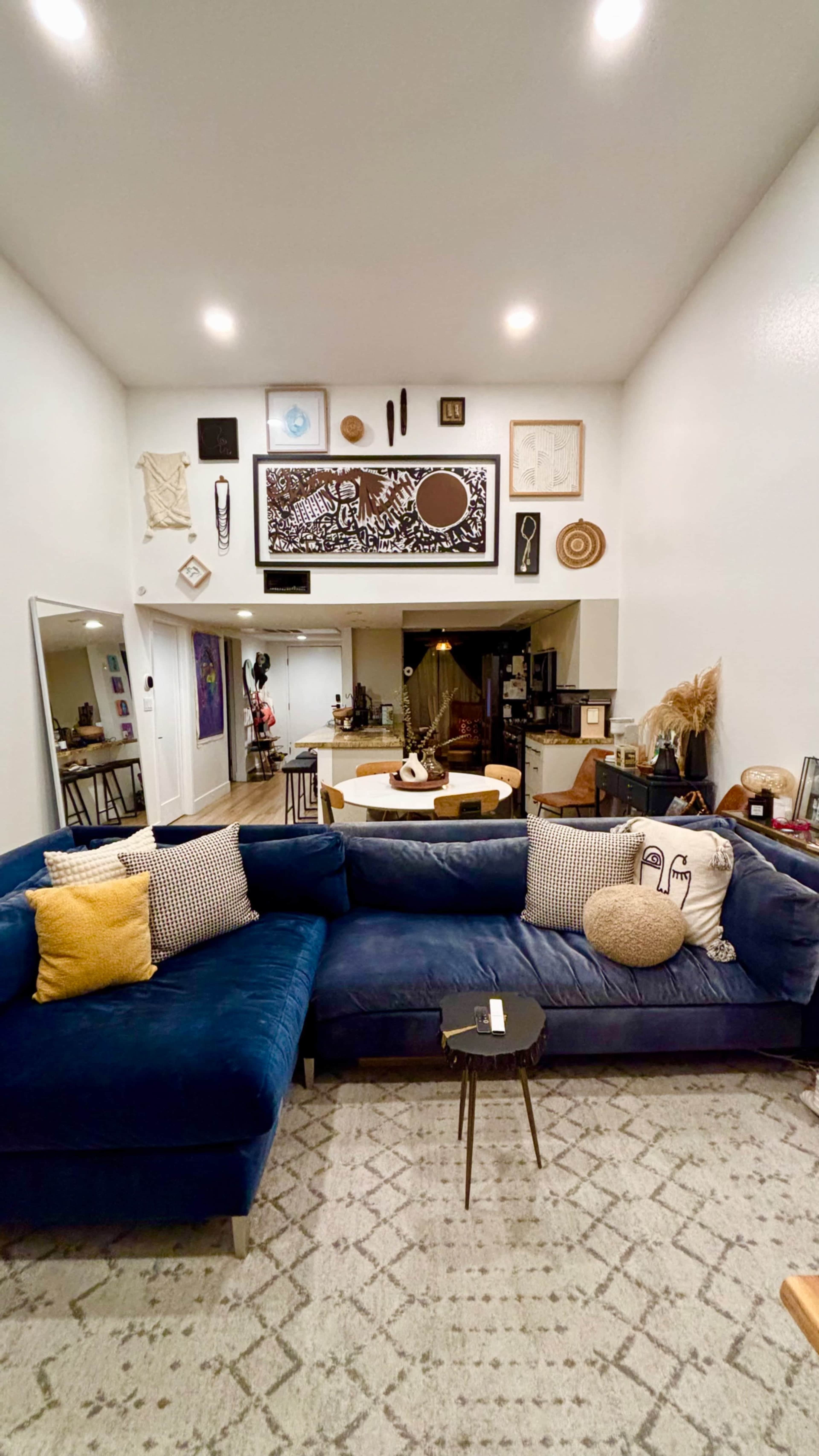 The image shows a modern living room with a blue sectional sofa, a small side table, and various artworks and decorative items on the walls.