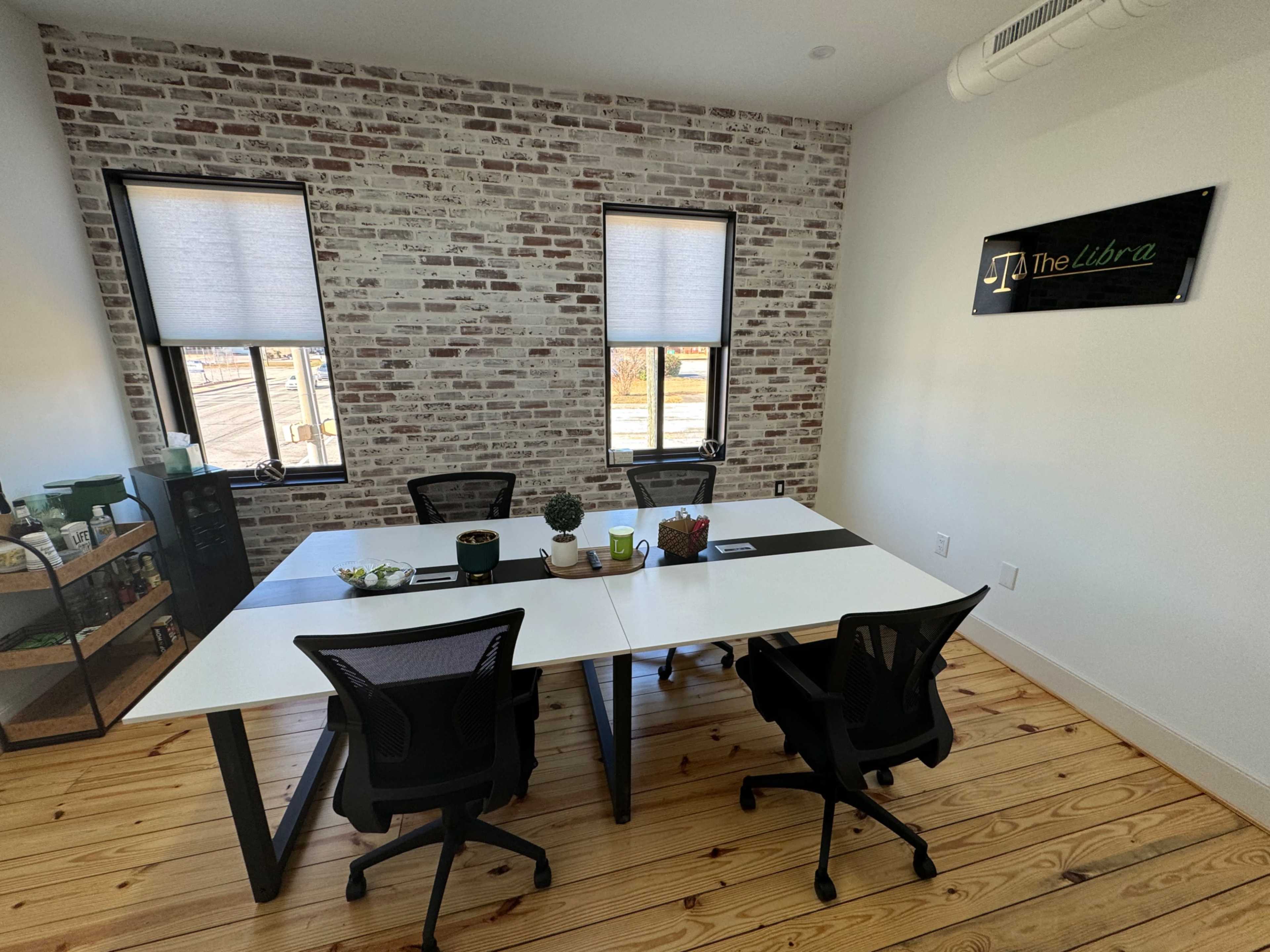 A modern office space with a white table, black chairs, exposed brick walls, and a sign reading "The Libra" on the wall.