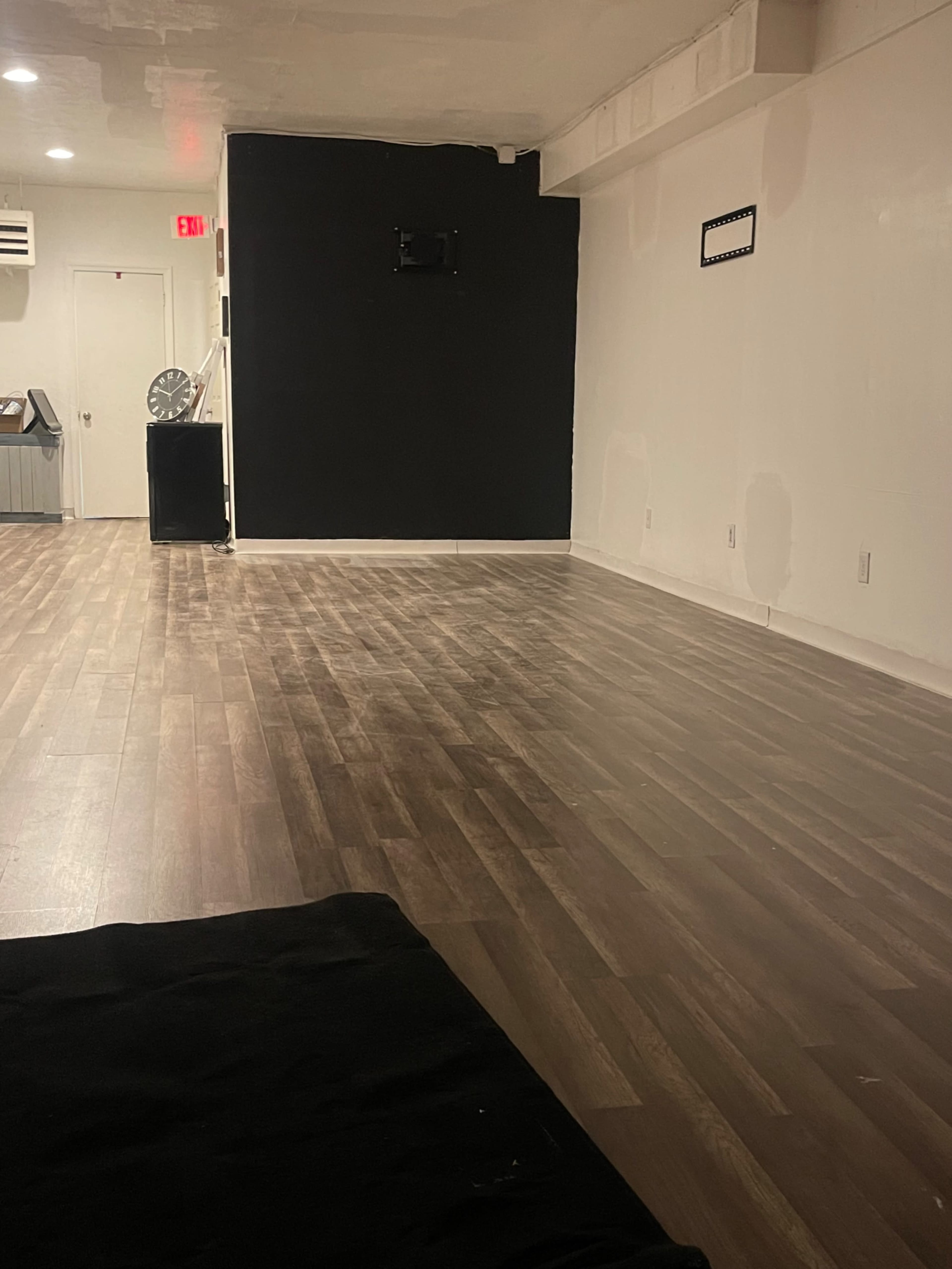 A spacious, mostly empty room with hardwood flooring, a black wall, and a door on one side.