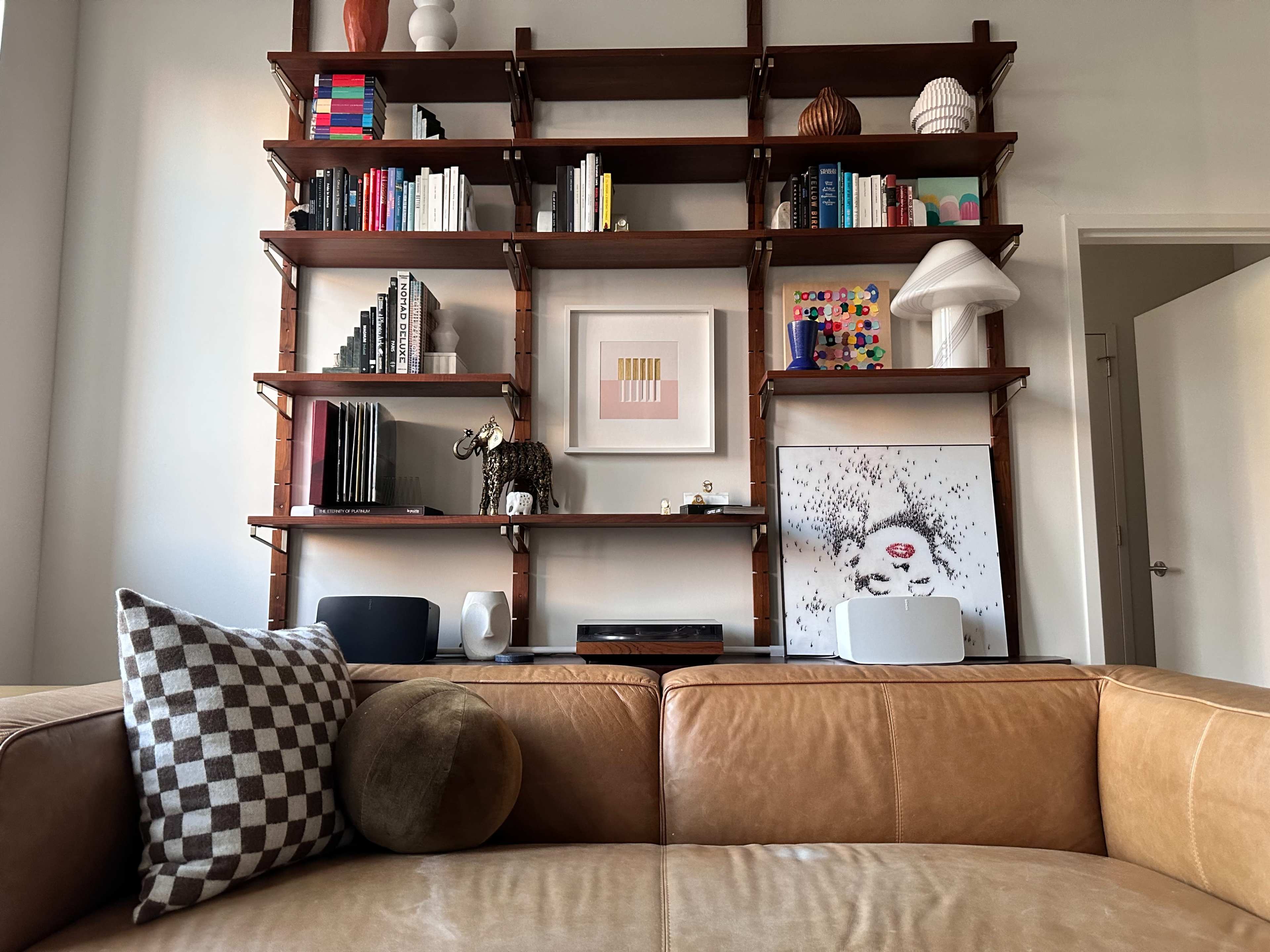 The image shows a living room scene featuring a leather couch in the foreground and a wooden bookshelf filled with various books, decorative items, and artworks in the background.