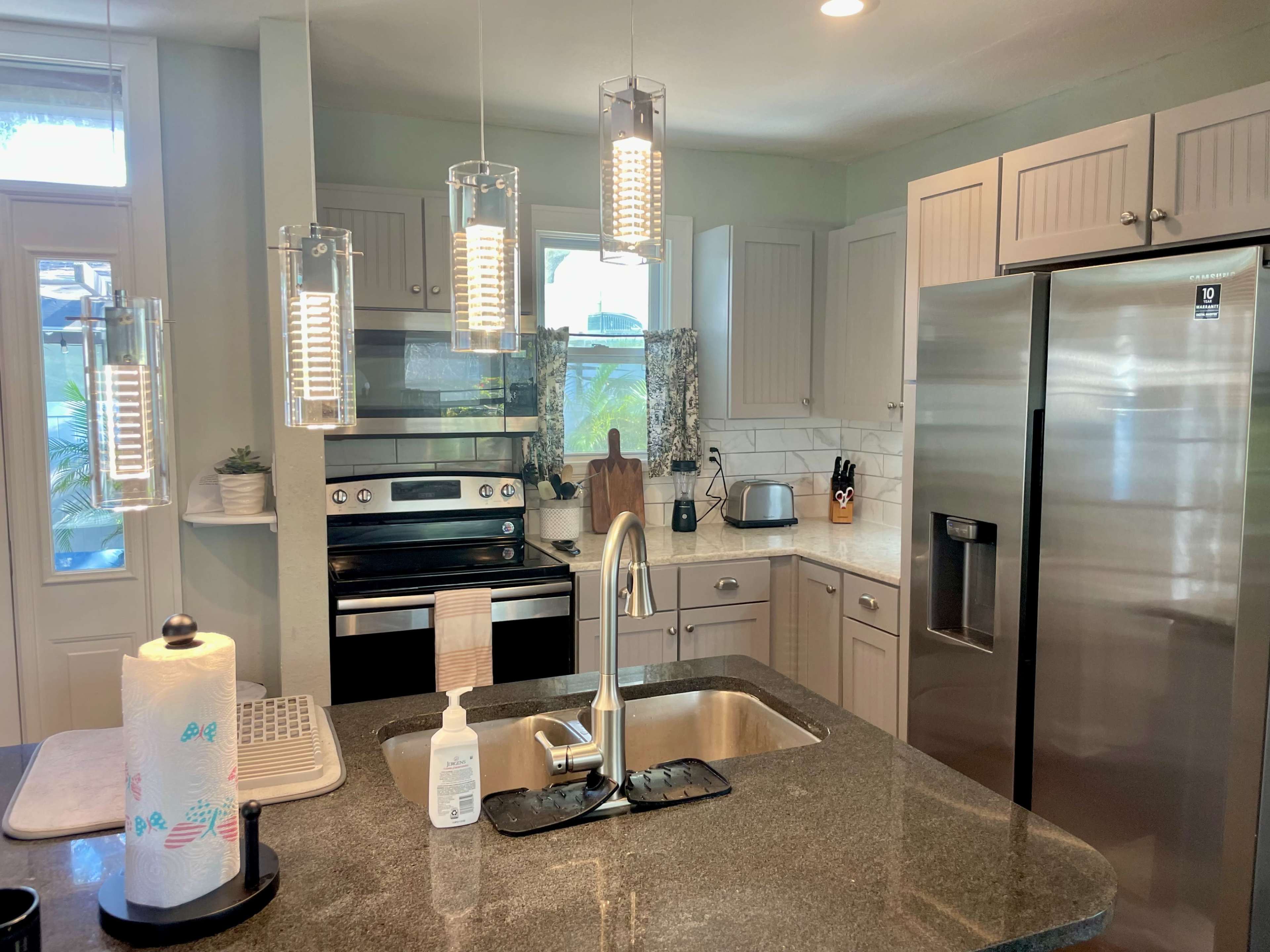 A modern kitchen with stainless steel appliances, gray countertops, and pendant lighting above the island.