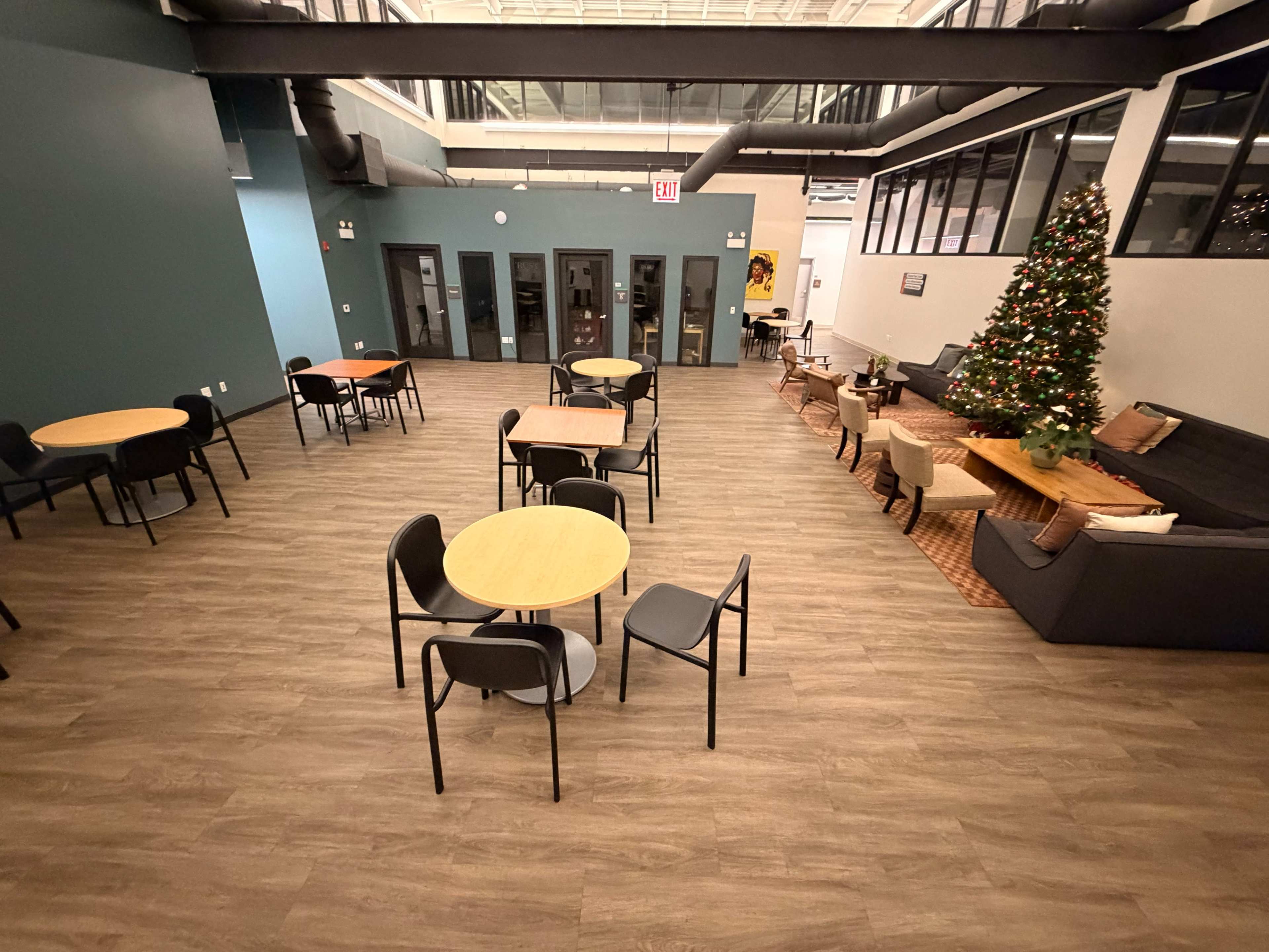 The image shows a modern indoor space with several round tables and chairs arranged around a plush couch and a Christmas tree in the corner.