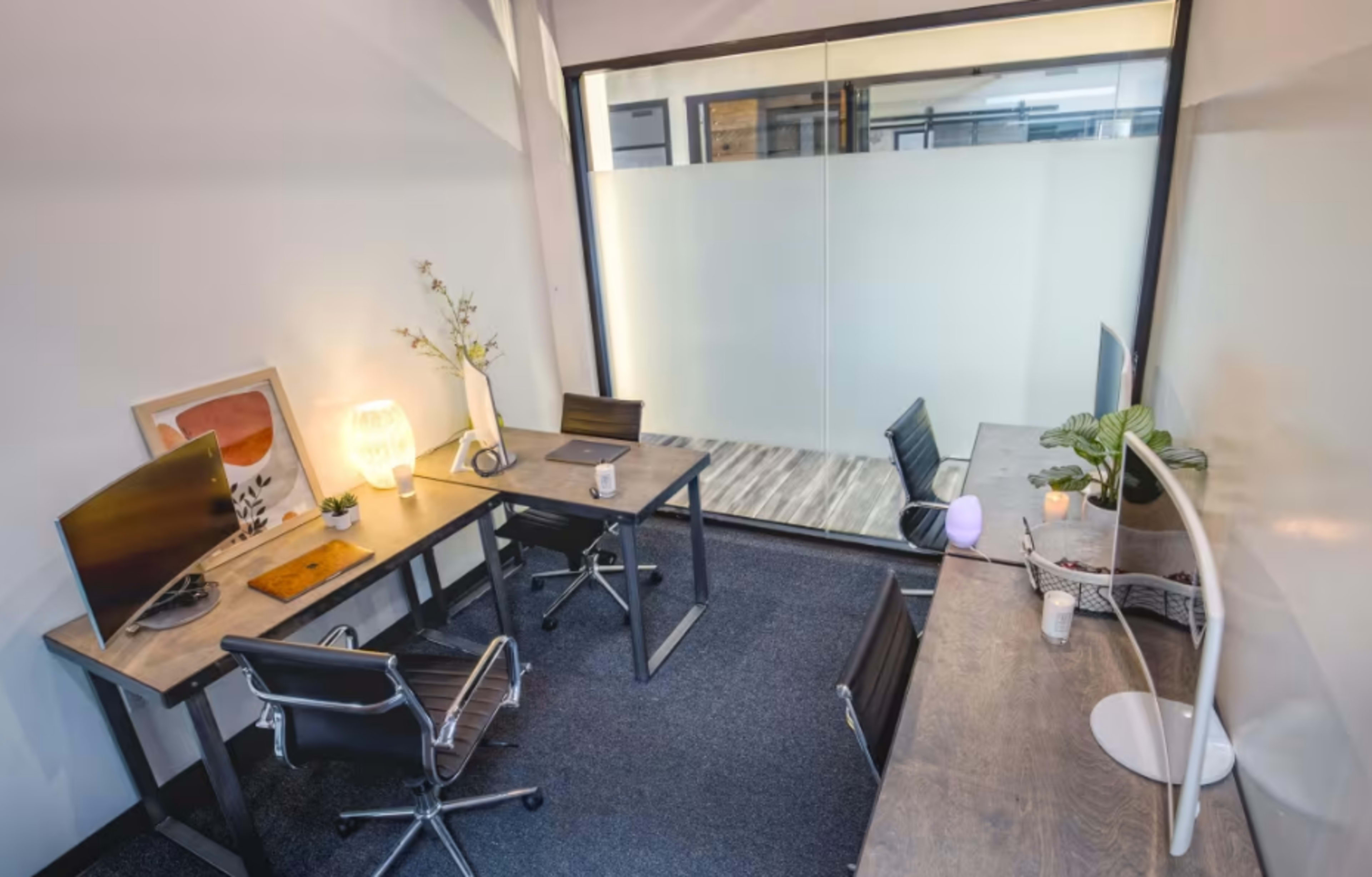The image shows a modern office space with two workstations, each equipped with monitors and office chairs, and a decorative lamp on one desk.