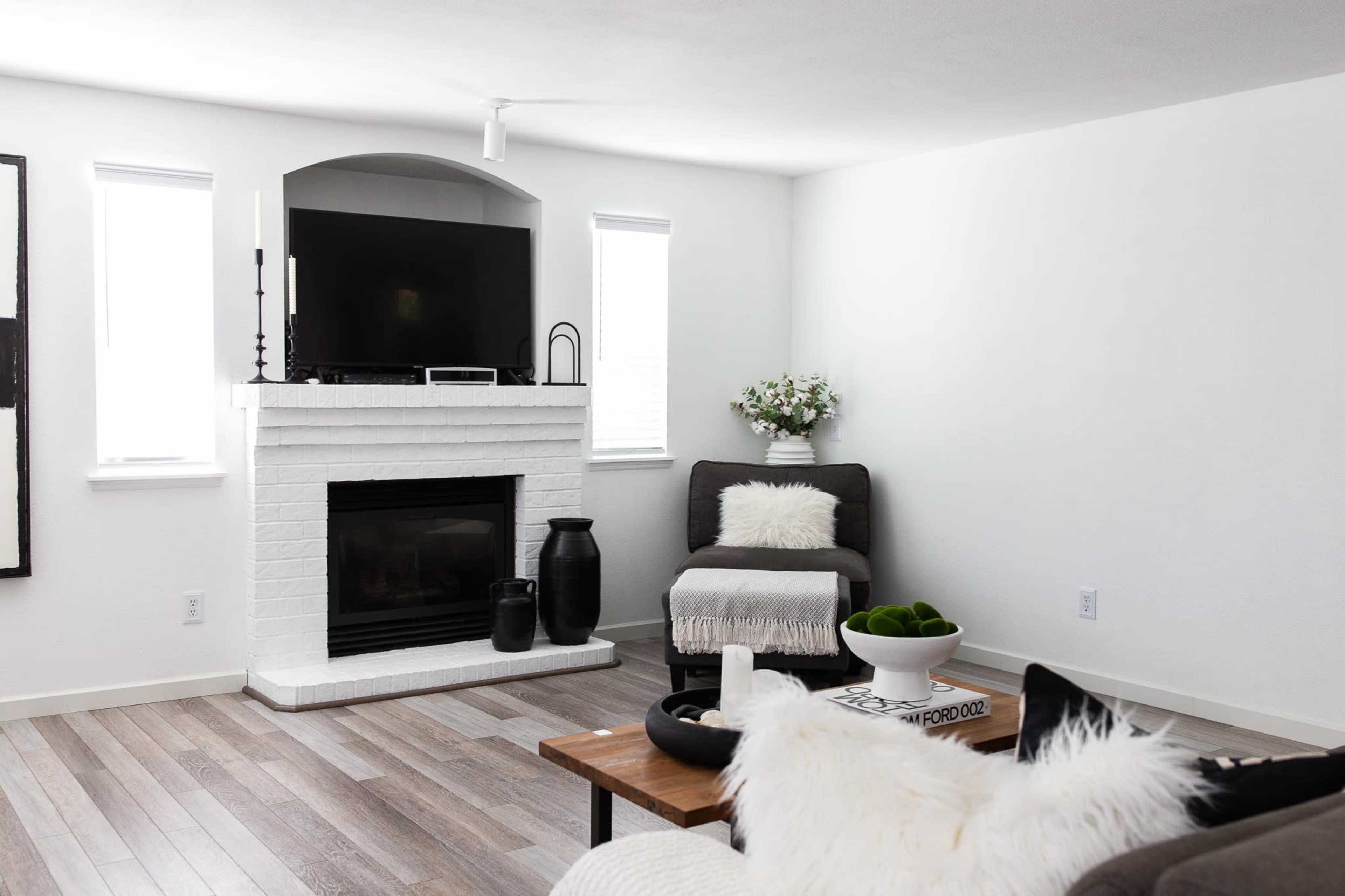 A modern living room with a white brick fireplace, a television mounted above it, and a seating area featuring a chair and a coffee table.