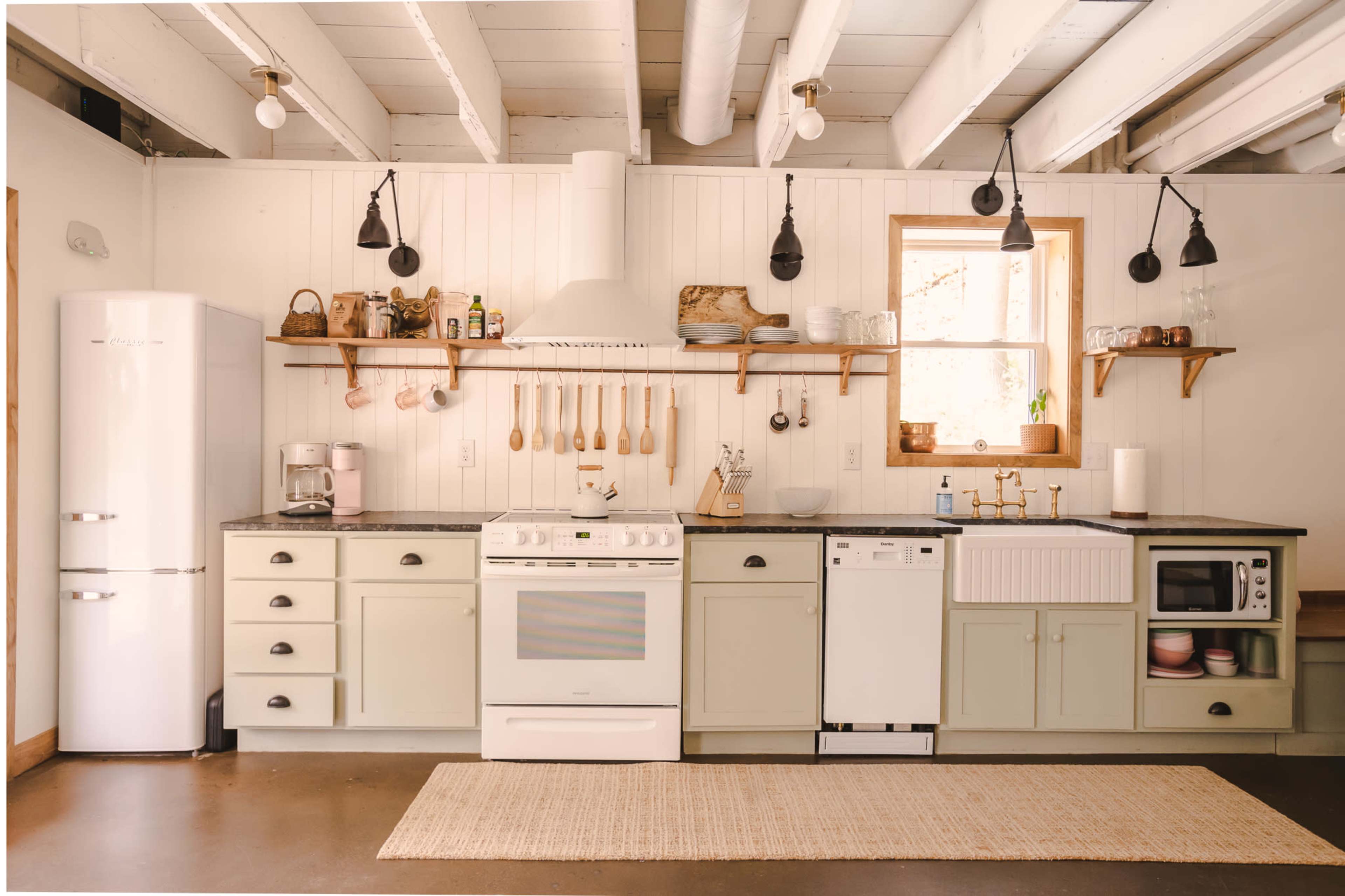 The kitchen features light green cabinetry, a white stove, a farmhouse sink, and various appliances arranged along a wooden countertop.