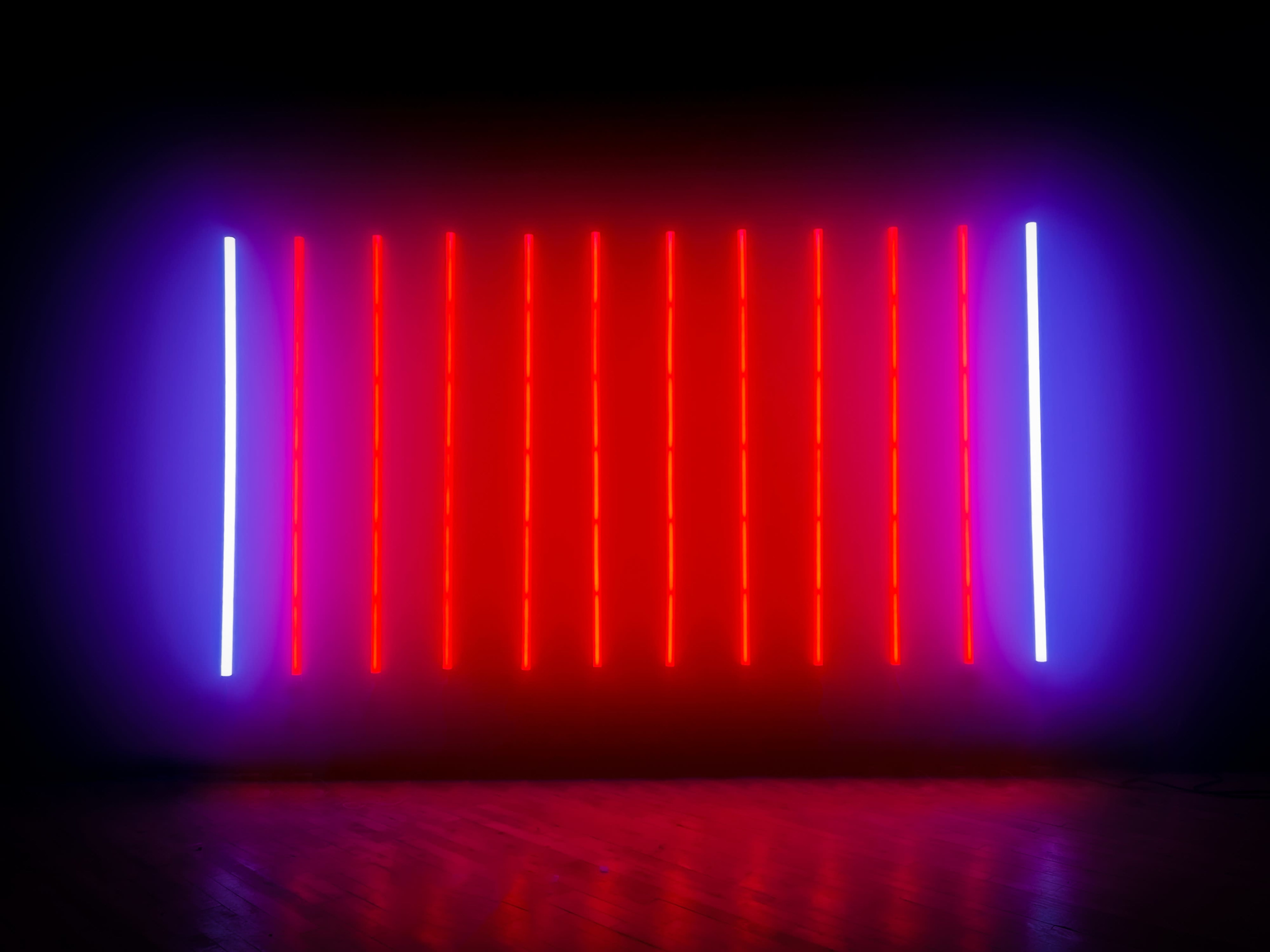 A wall is illuminated with vertical neon light strips in red and blue.