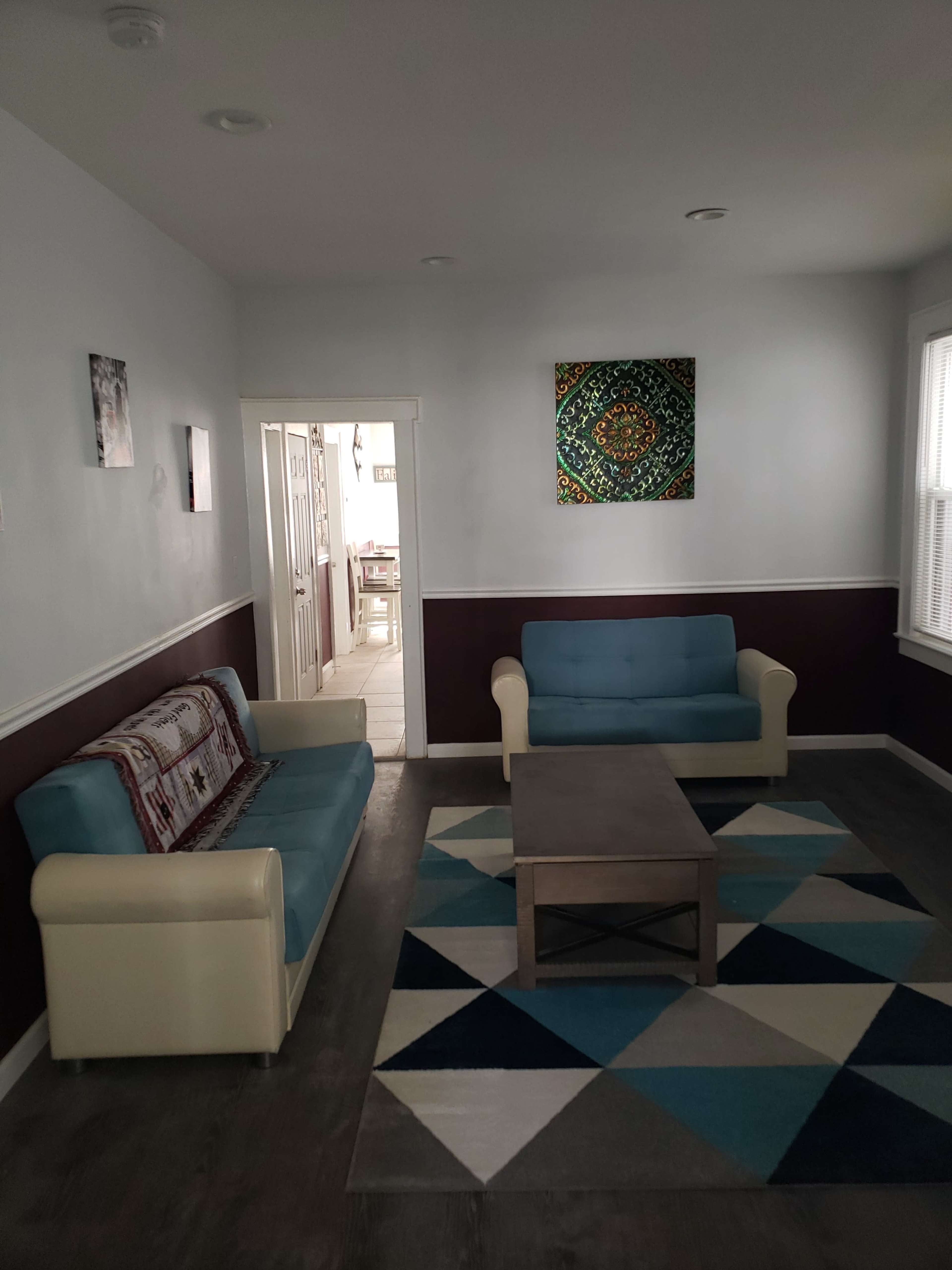 A living room with two light blue couches, a gray coffee table, and a patterned area rug, along with a doorway leading to another room.