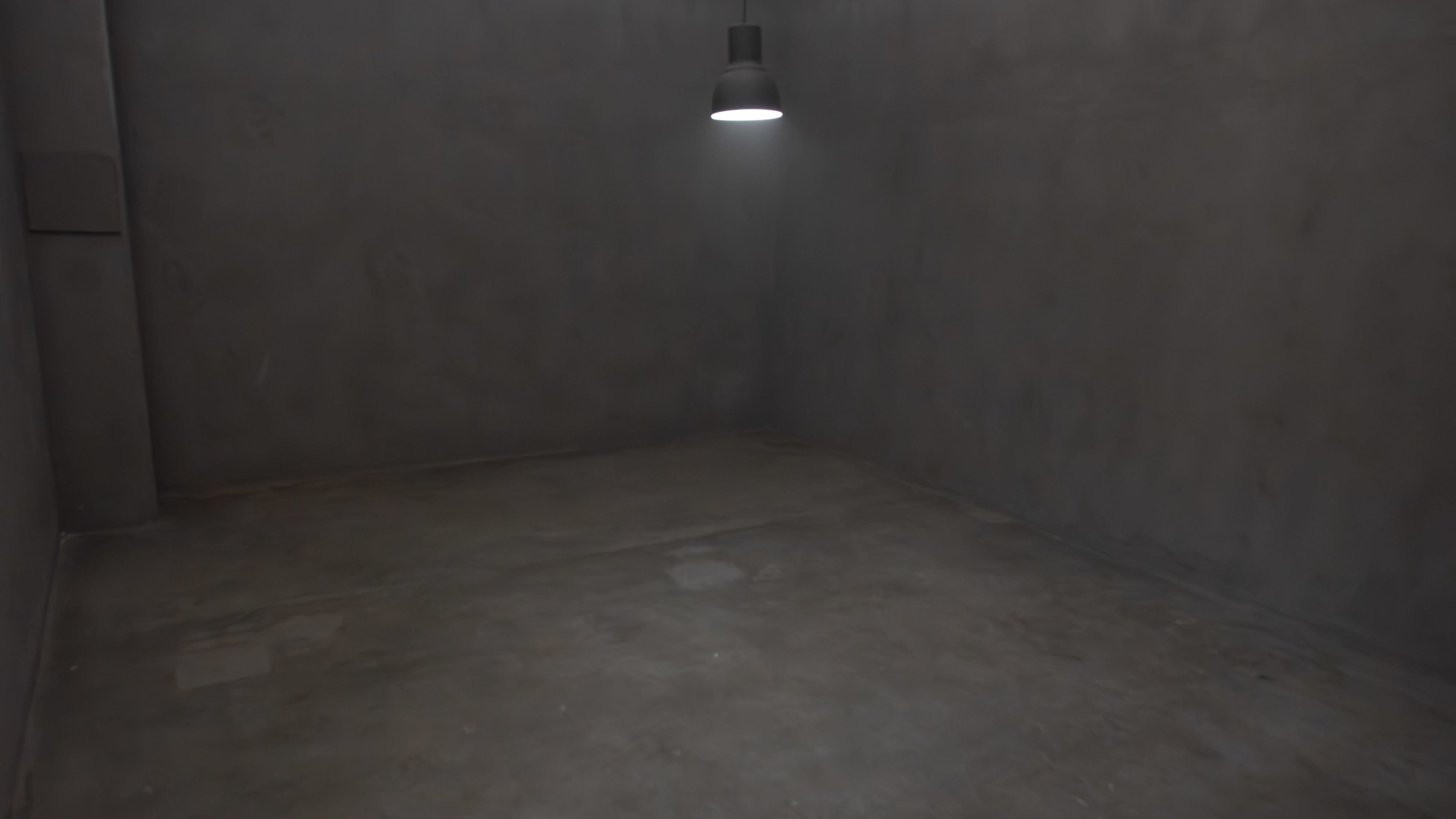 An empty, dimly lit concrete room with a single overhead light in one corner.
