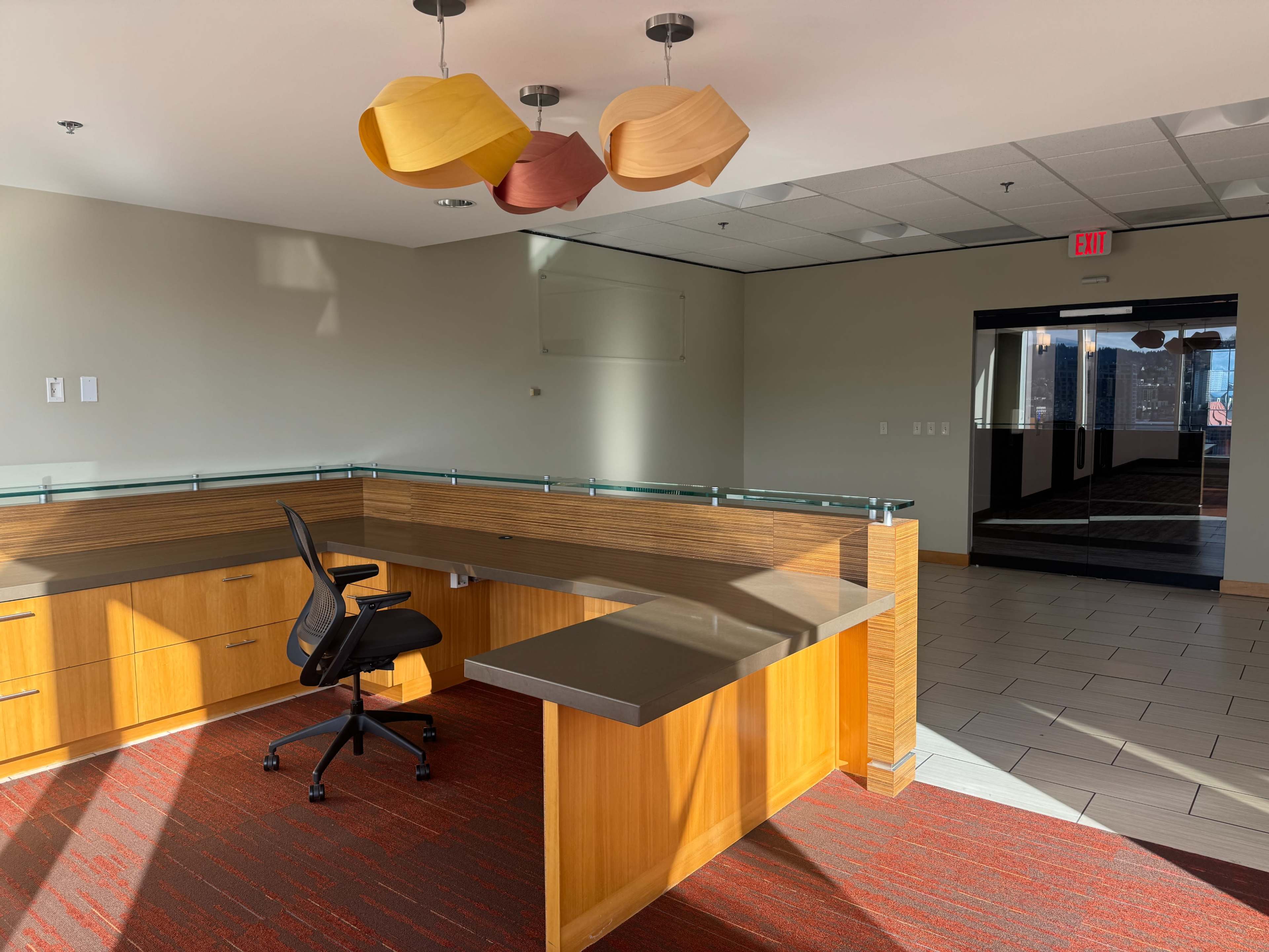 The image shows a modern office space with a wooden reception desk, a spinning chair, and decorative light fixtures hanging from the ceiling.