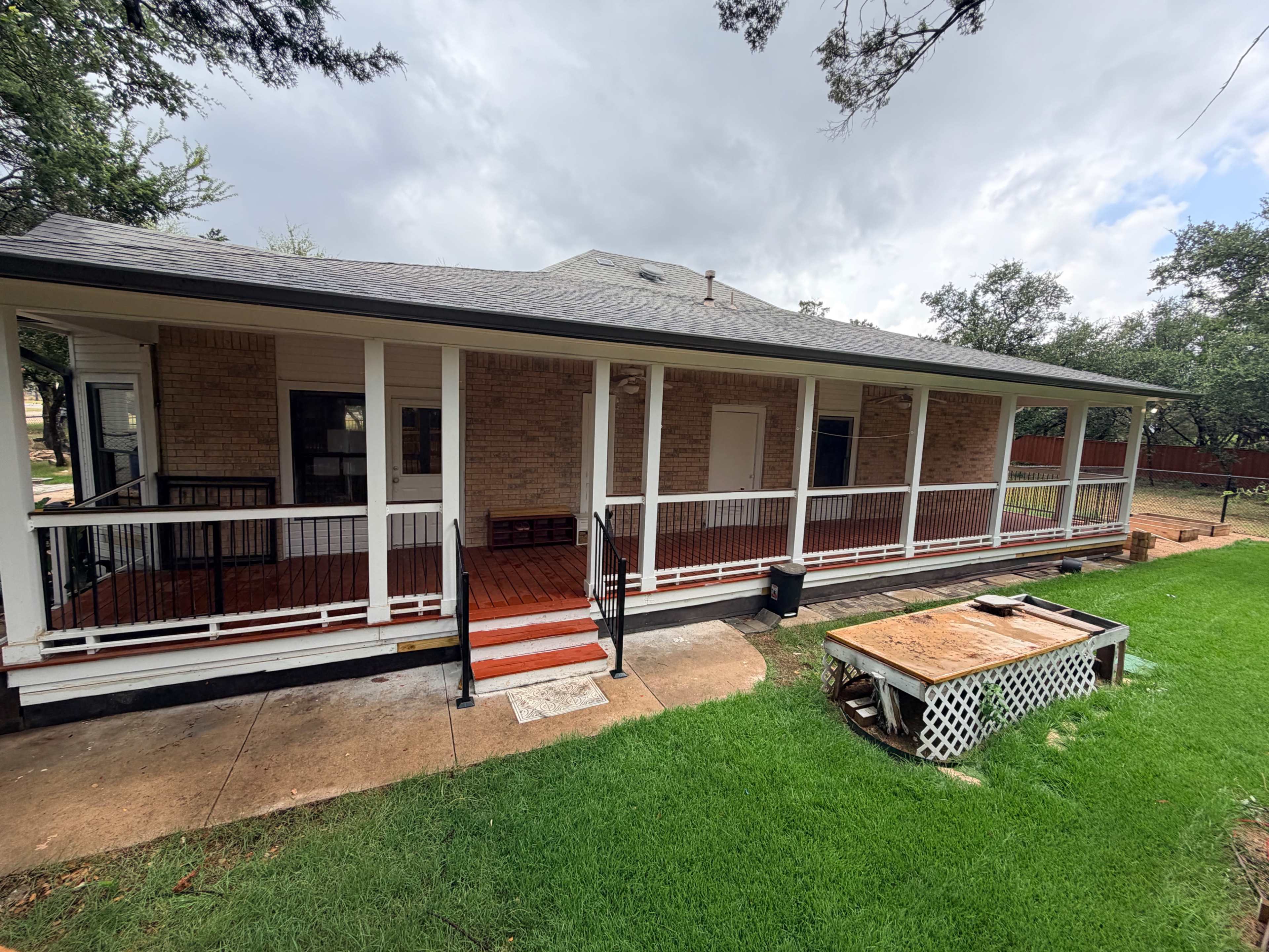 The image shows a single-story brick house with a covered porch and a large grassy yard.