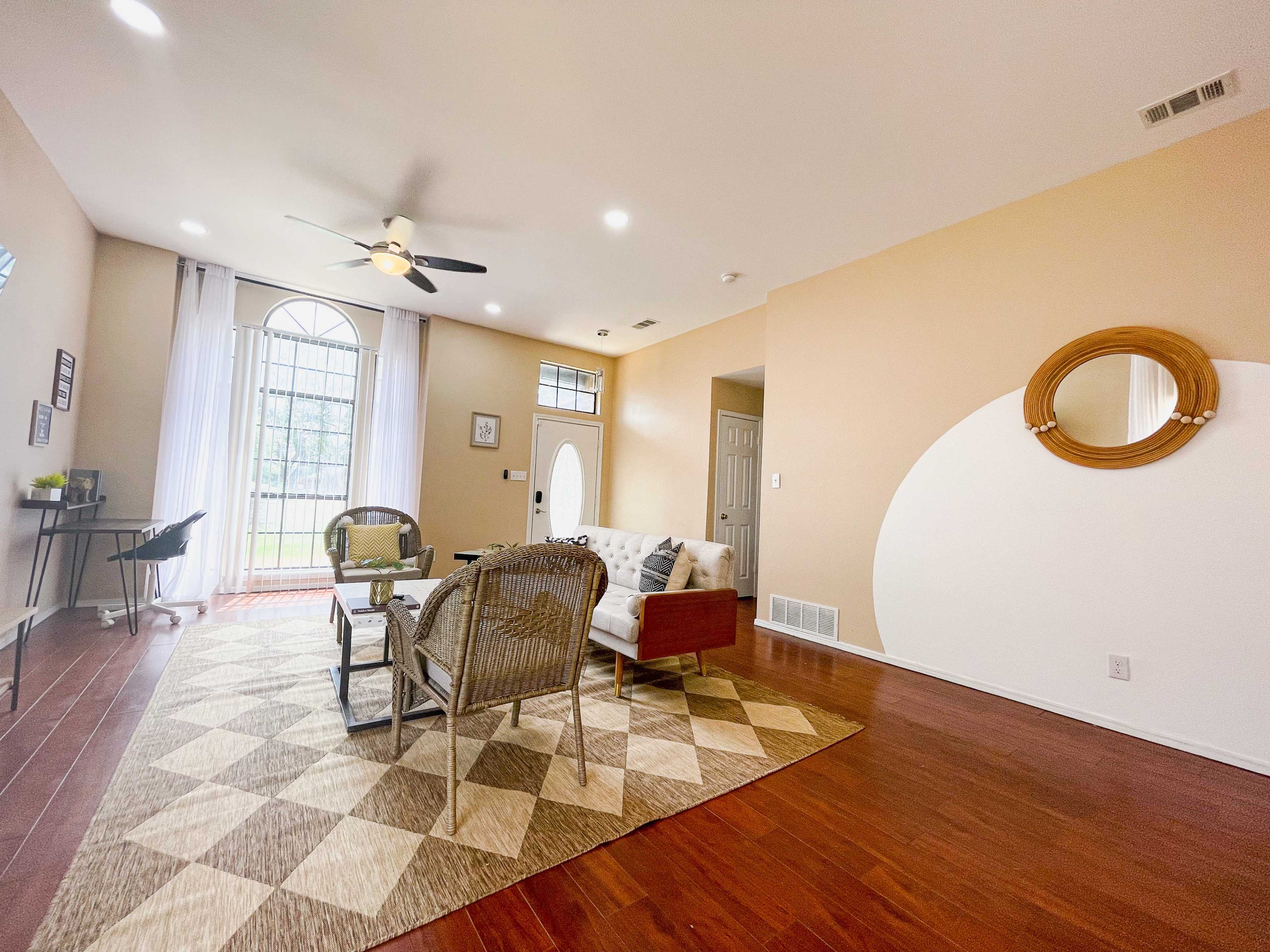 The living room features a light-colored sofa and chairs arranged on a patterned area rug, with large windows providing natural light.