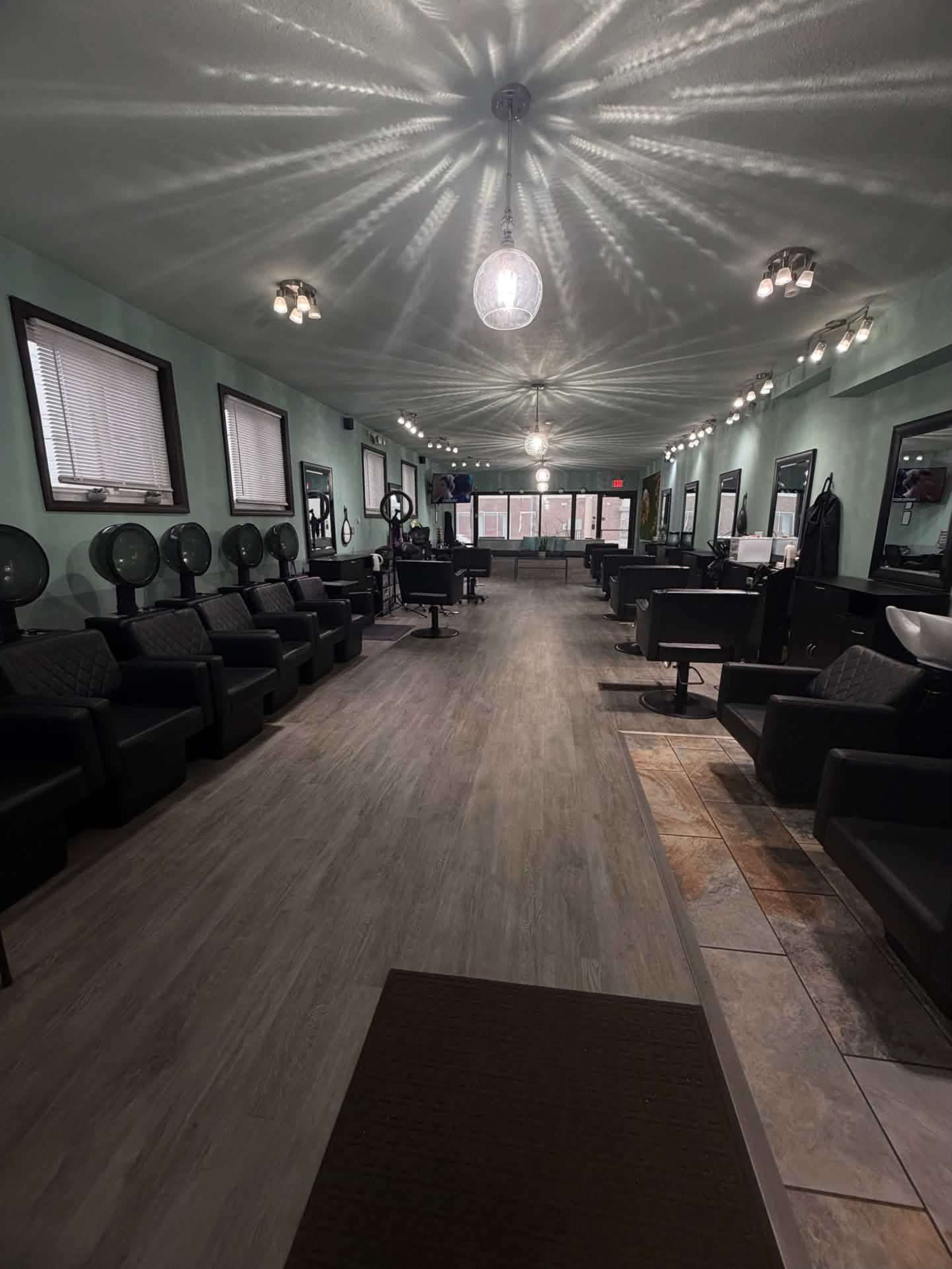 The image shows the interior of a hair salon featuring several styling stations, black chairs, and hairdryers arranged along the walls under soft lighting.