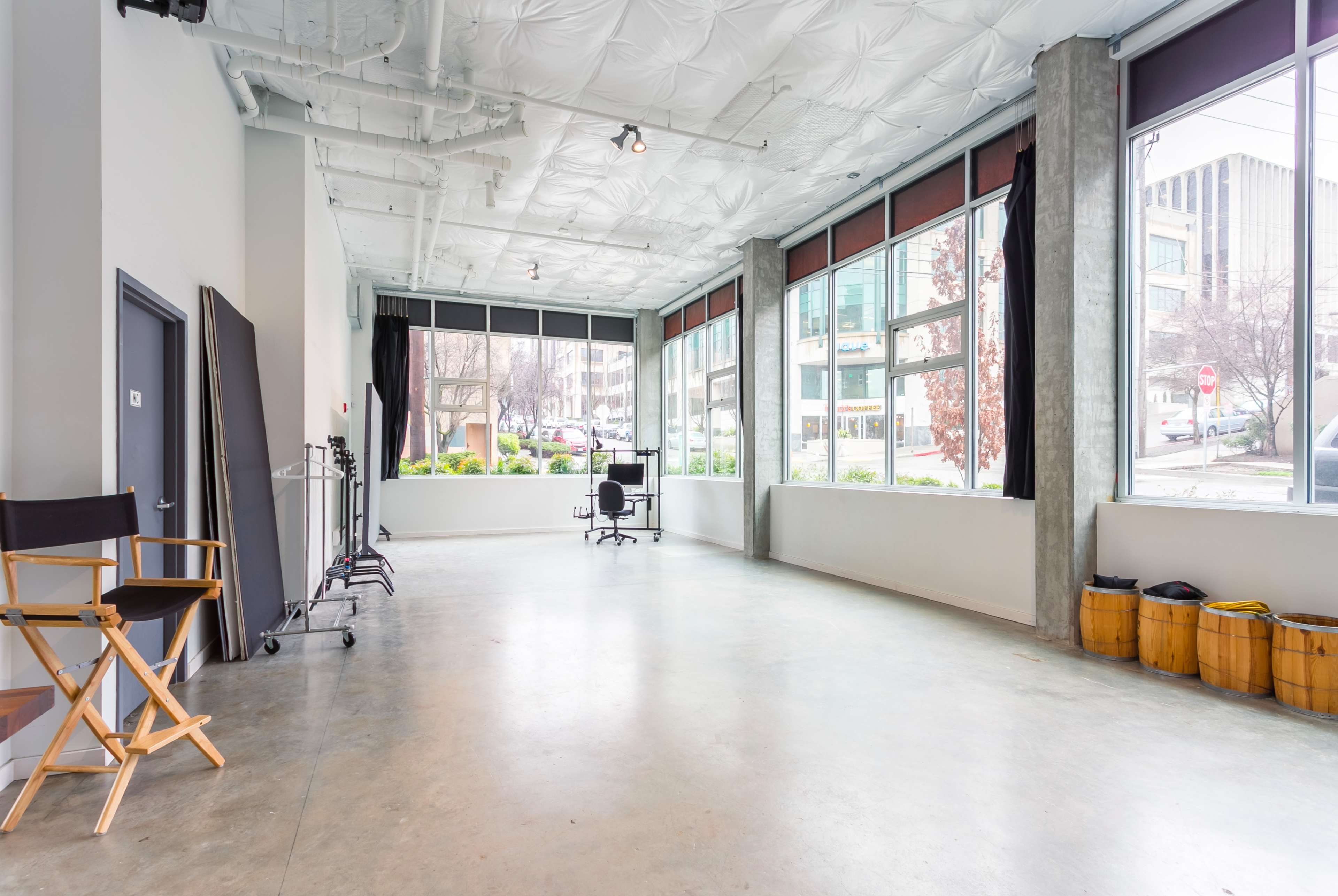 A spacious, well-lit studio features large windows, a chair at the center, and a filming setup on one side.