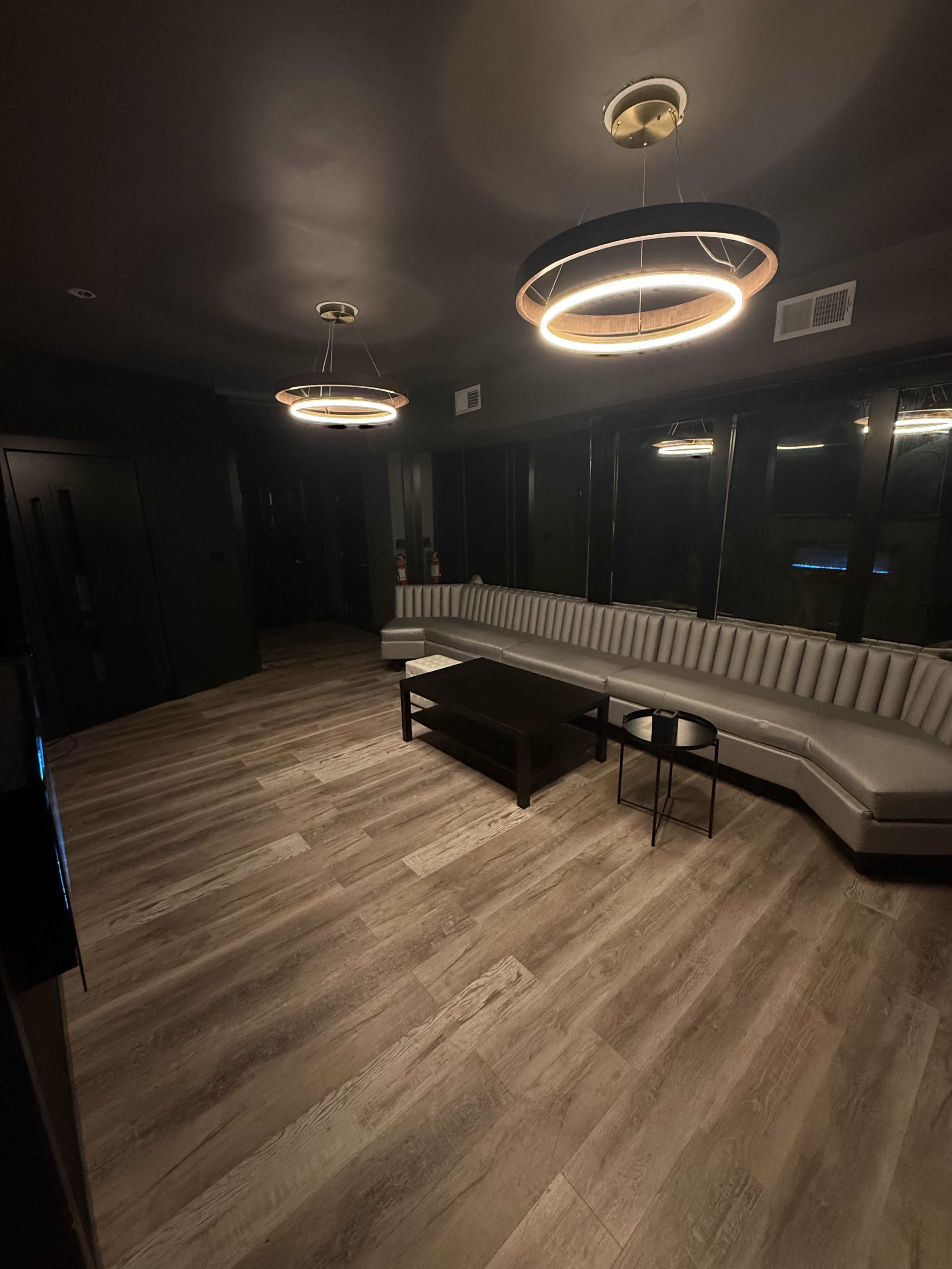 The image shows a modern, minimalist room featuring a curved gray couch, a black coffee table, and circular ceiling lights.