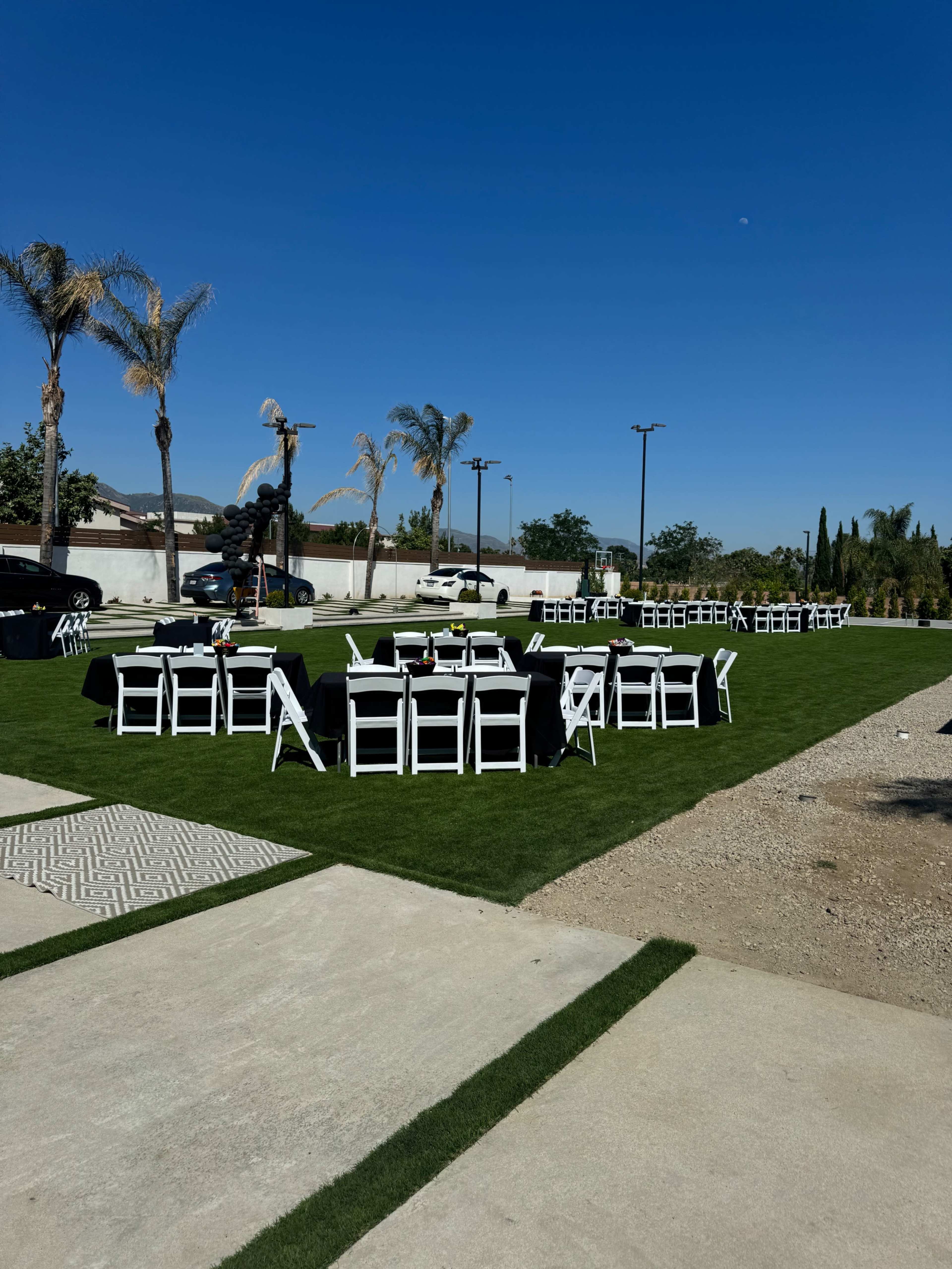 A setup for an outdoor event with several tables and chairs arranged on a grassy area under a clear blue sky.