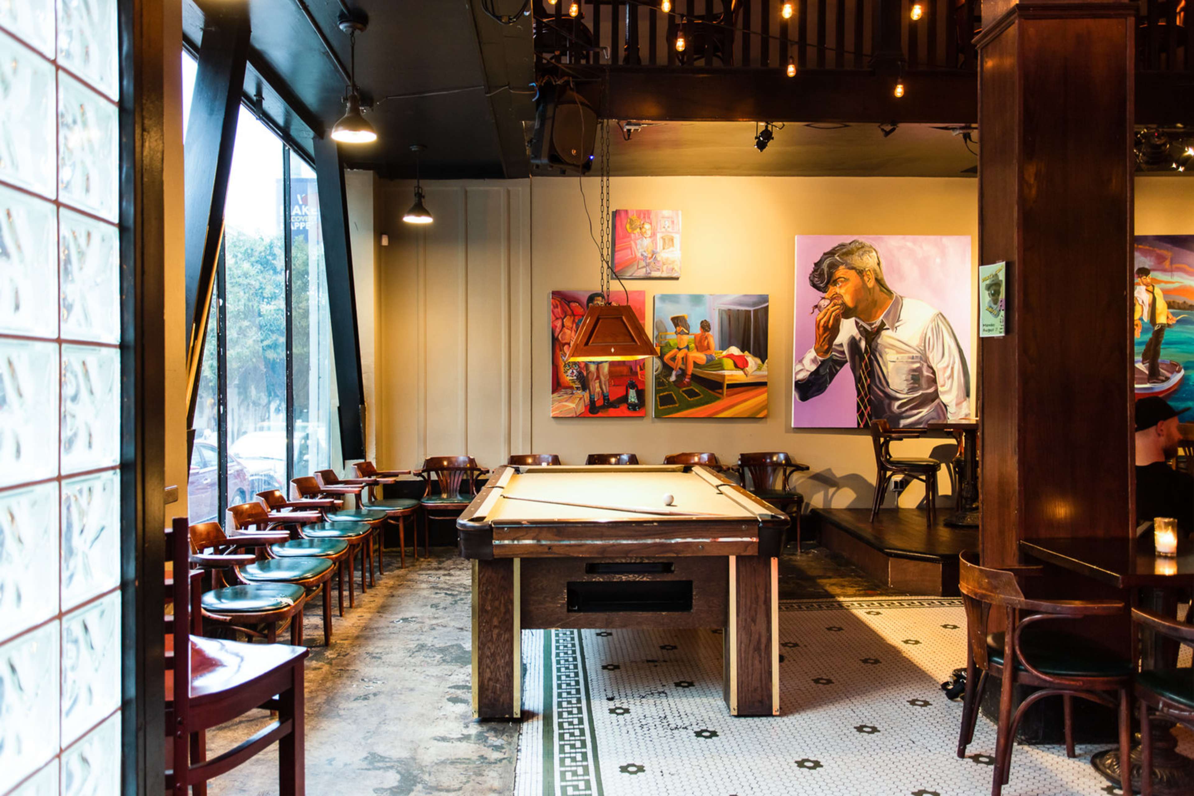 A bar or lounge area featuring a pool table in the center, surrounded by chairs and adorned with vibrant artwork on the walls.
