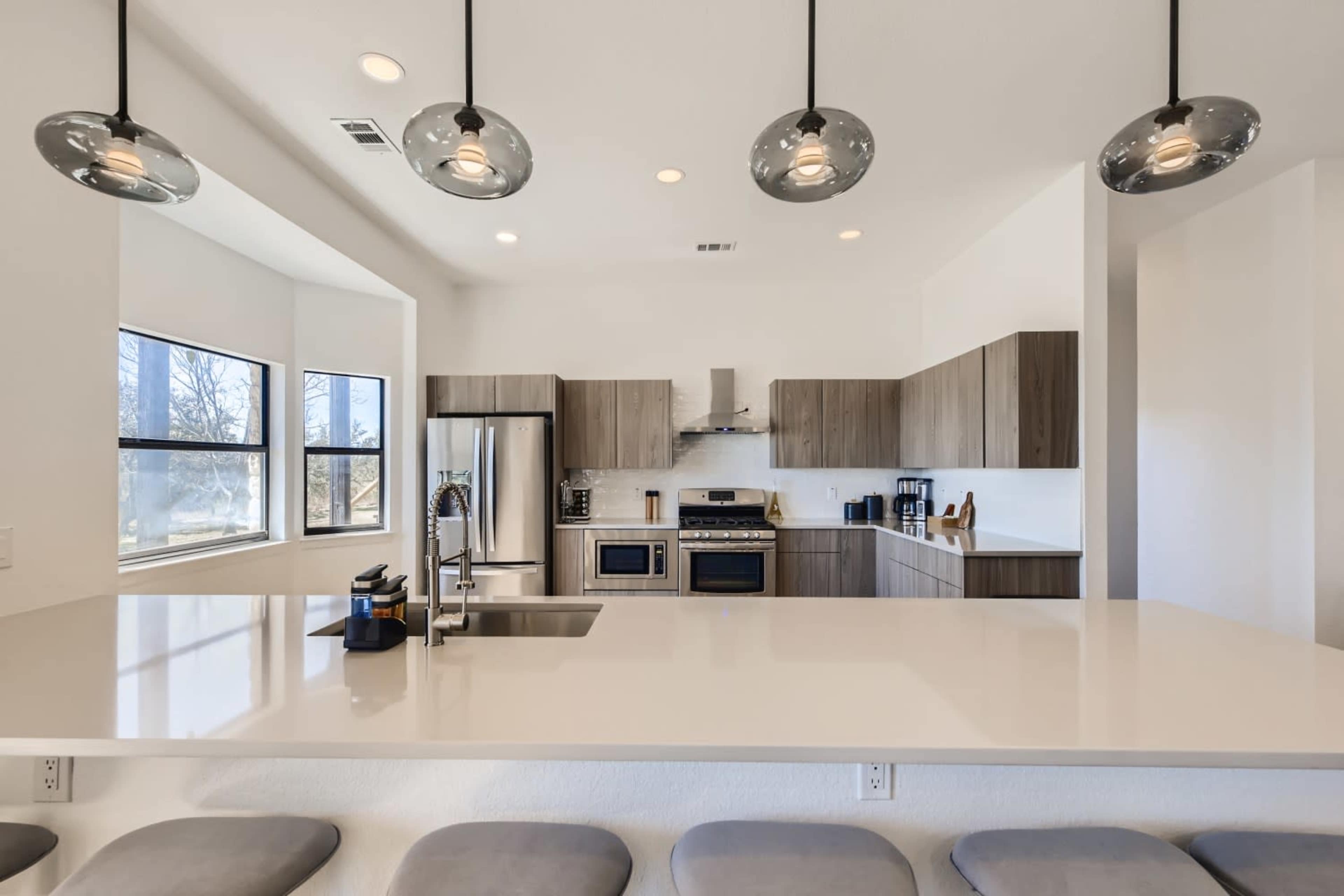 A modern kitchen with wooden cabinets, stainless steel appliances, and a sleek countertop with pendant lighting.