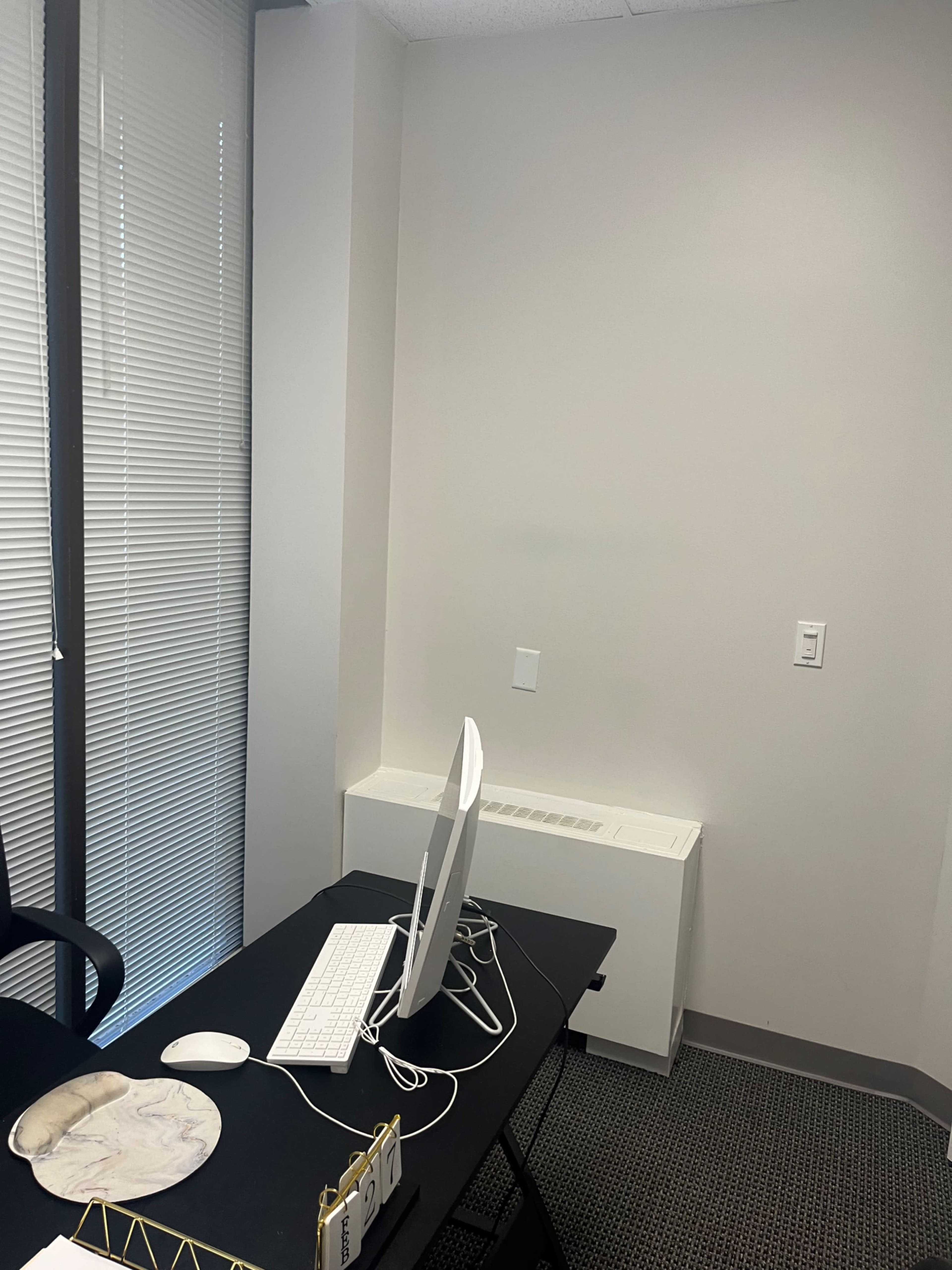 The image shows a minimalistic office space with a black desk, a computer monitor, and a keyboard positioned against a light-colored wall.