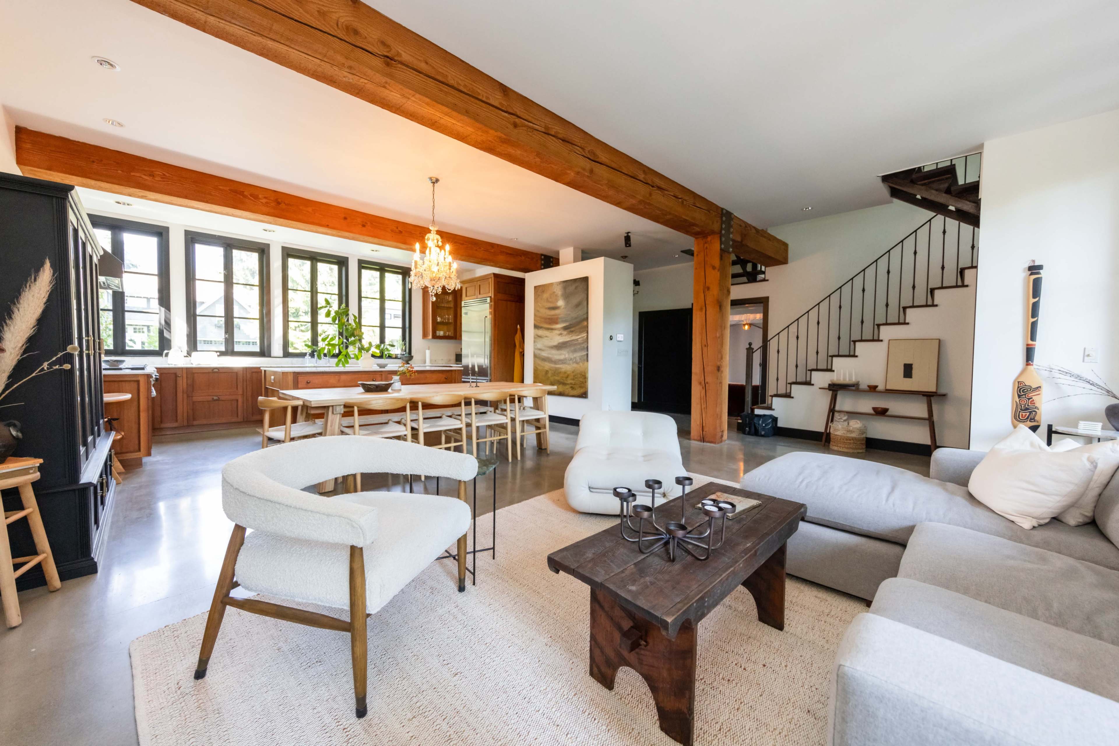 A modern open-concept living space featuring a dining area, comfortable seating, and a staircase.