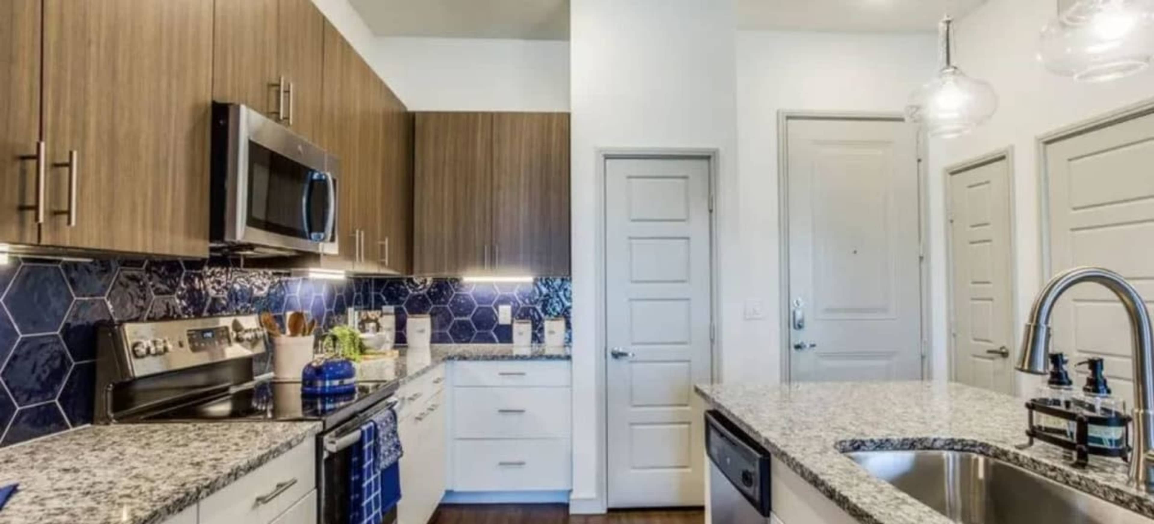 A modern kitchen featuring wood-panelled cabinets, granite countertops, stainless steel appliances, and a hexagonal tile backsplash.
