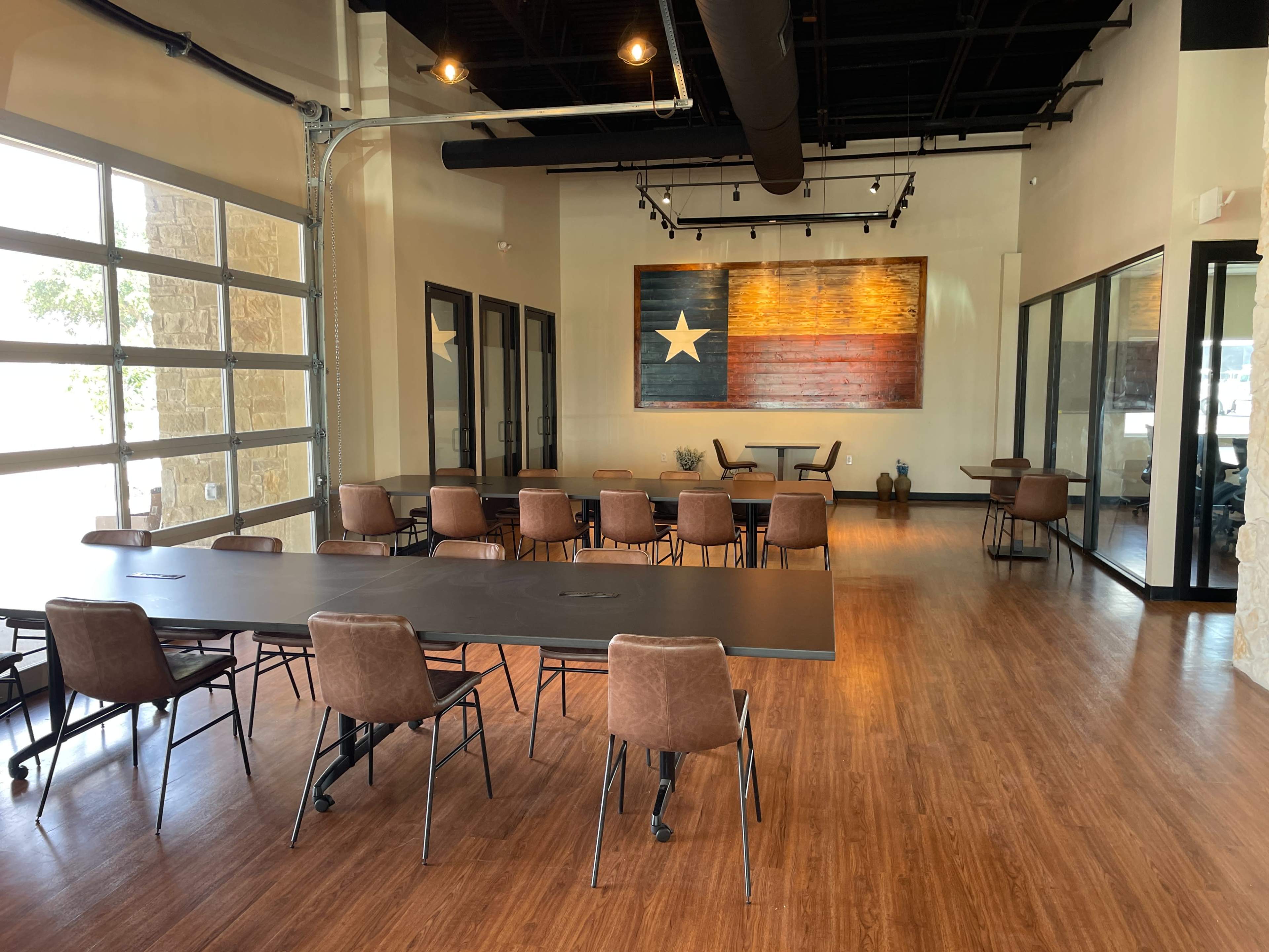 A spacious meeting room features several tables and chairs, with large windows and a large wall art displaying a star and stripes design.